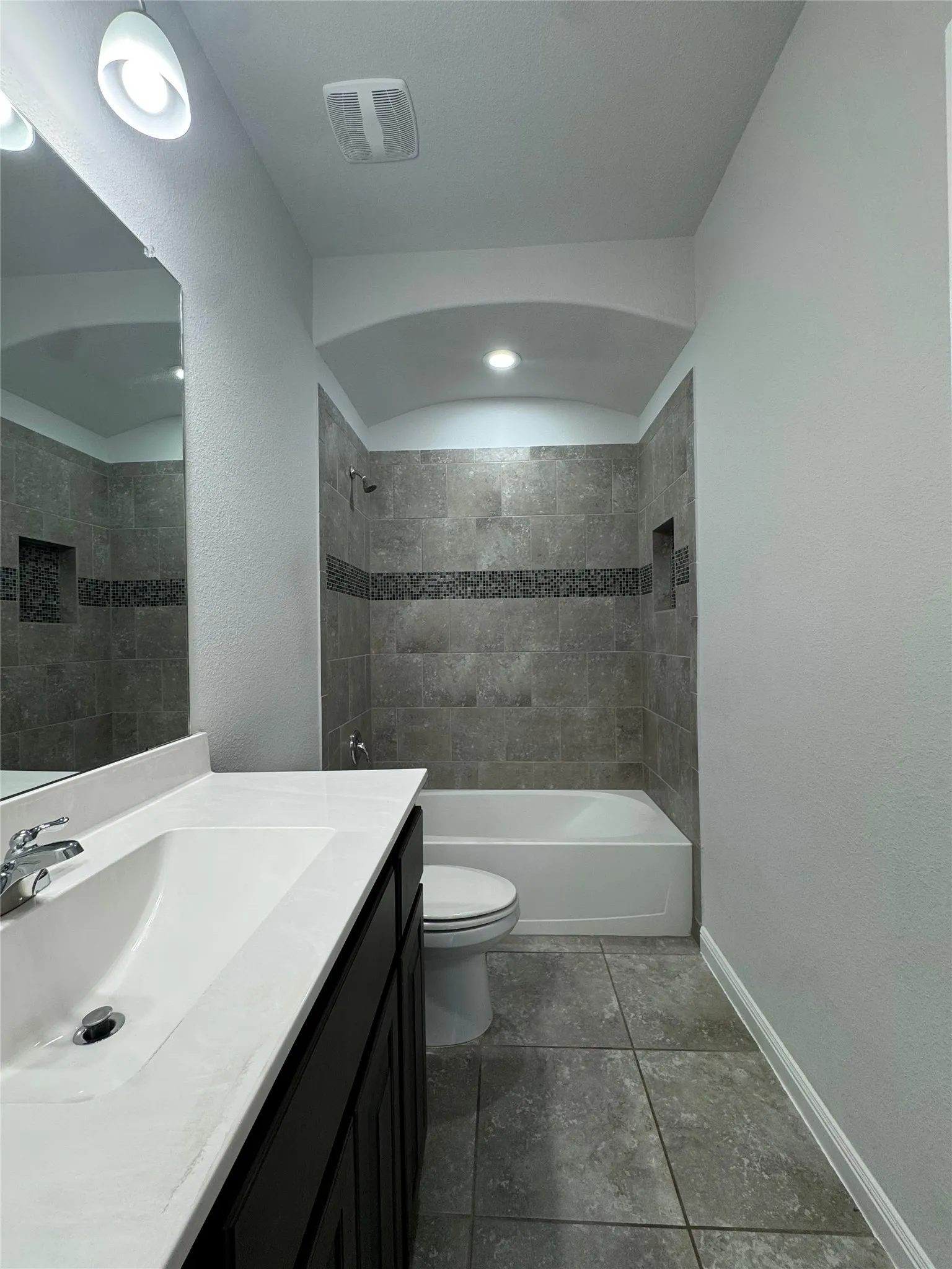 Bathroom featuring a vanity with an integrated sink, shower-over-tub with tile surround, decorative tile band, and arched ceiling detail