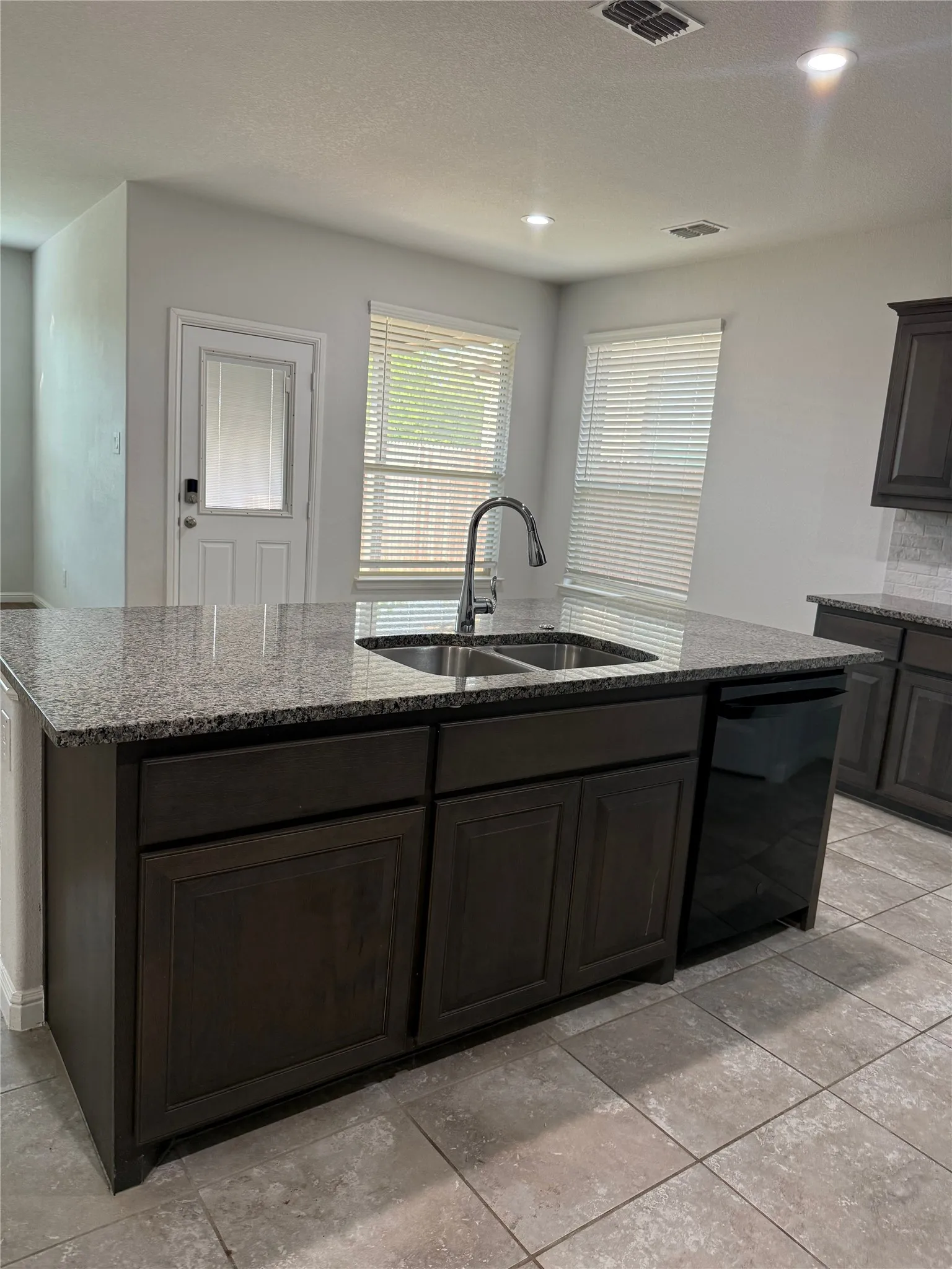Kitchen island featuring a dual basin sink with a gooseneck faucet, dark cabinetry, and a granite-finish countertop