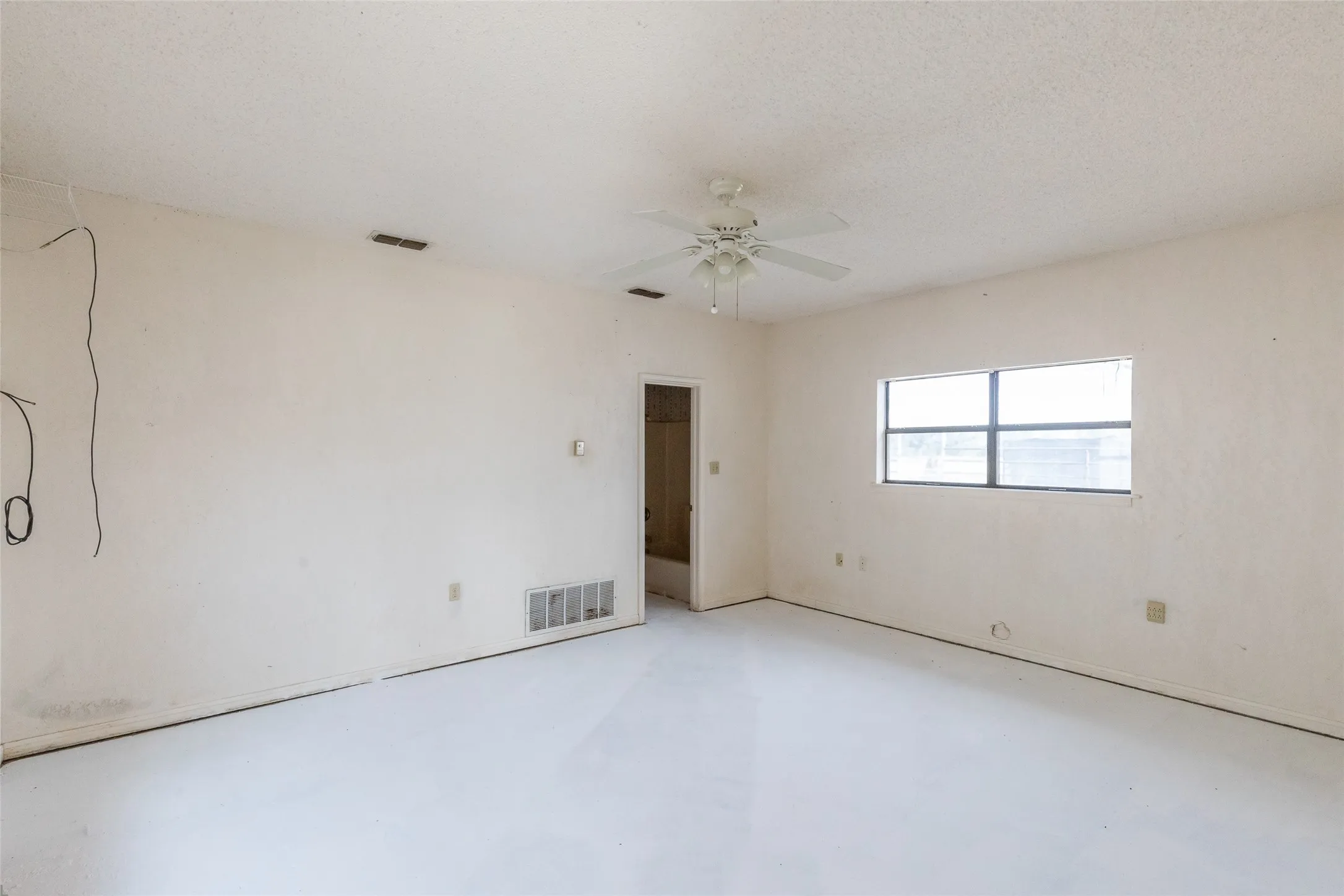 Spacious room featuring light-colored flooring, neutral wall tones, a ceiling fan with integrated lighting, and a large window