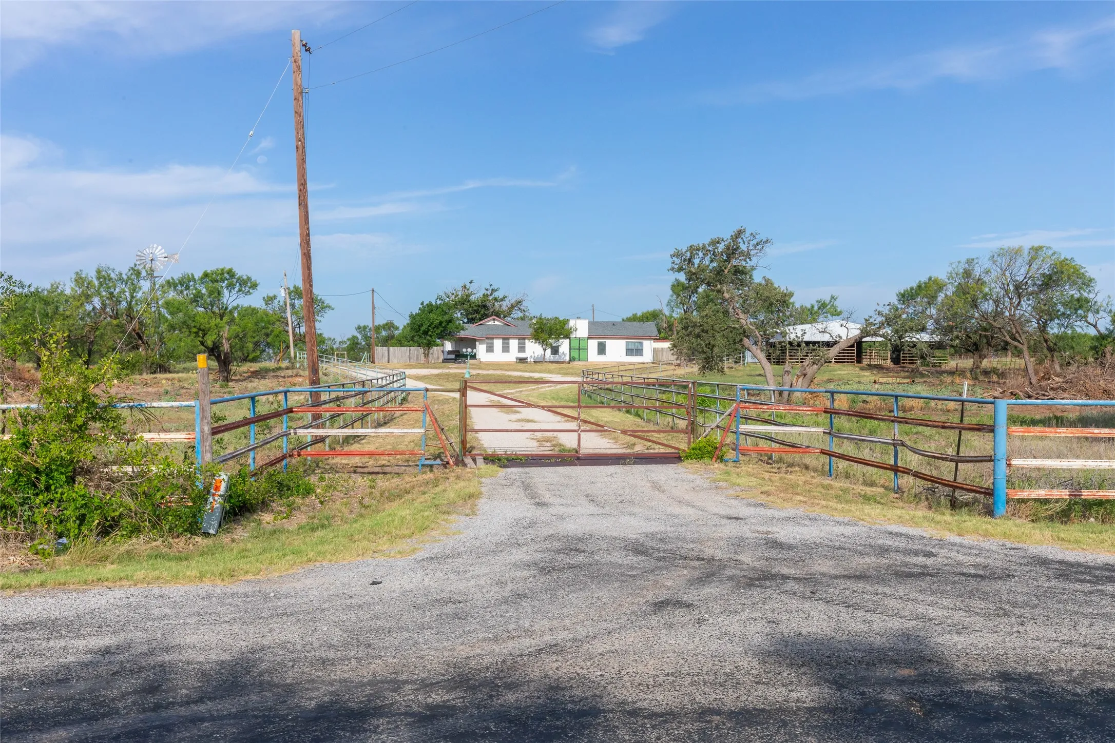 Gravel driveway leading to a gated entry with multiple fenced areas