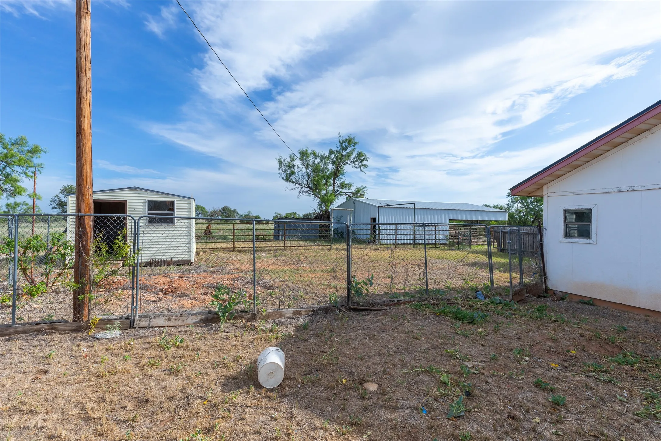 Expansive outdoor space featuring a chain-link fence and gate, a detached storage shed, and a large metal barn structure