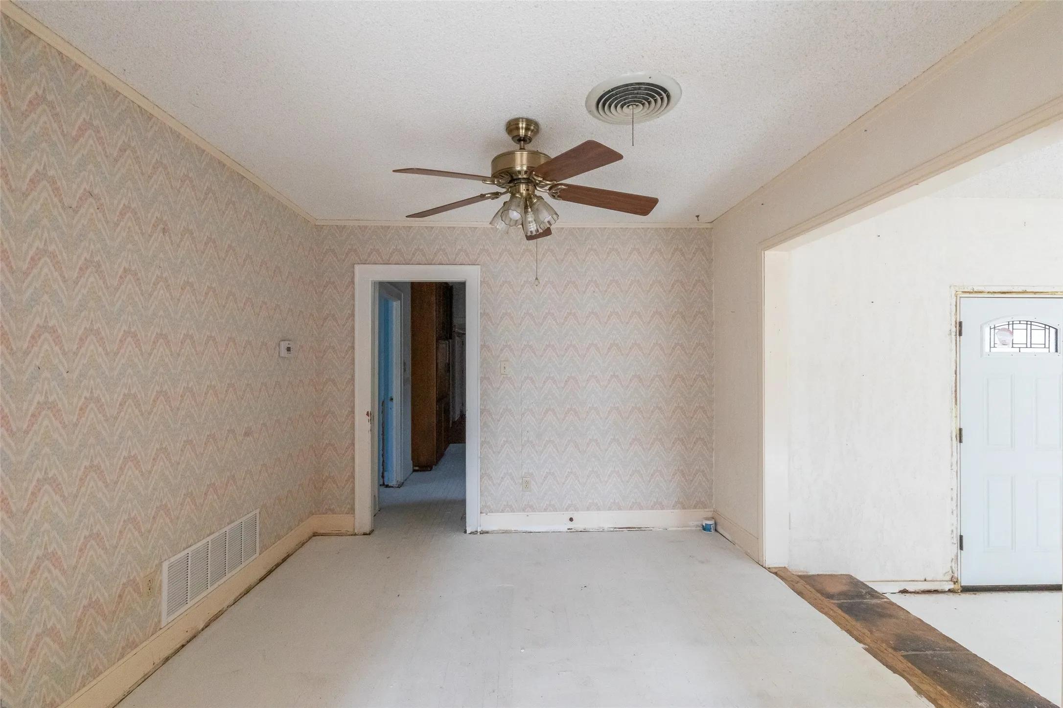 Interior space featuring patterned wallpaper, a ceiling fan with wood-look blades, and a white paneled door with decorative glass inserts
