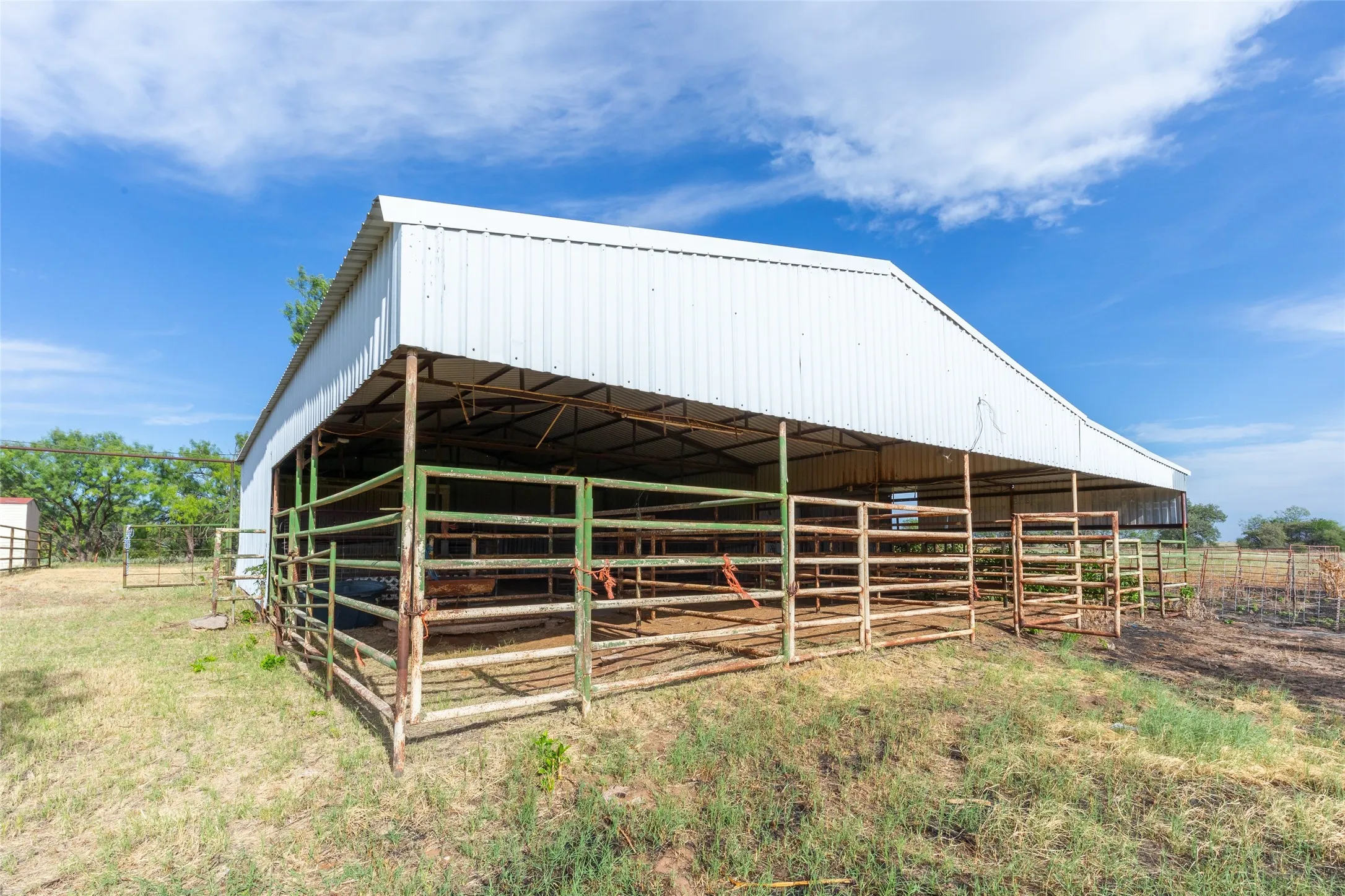 Metal-sided barn featuring a white corrugated roof, open-air stalls with metal fencing, and a large covered structure