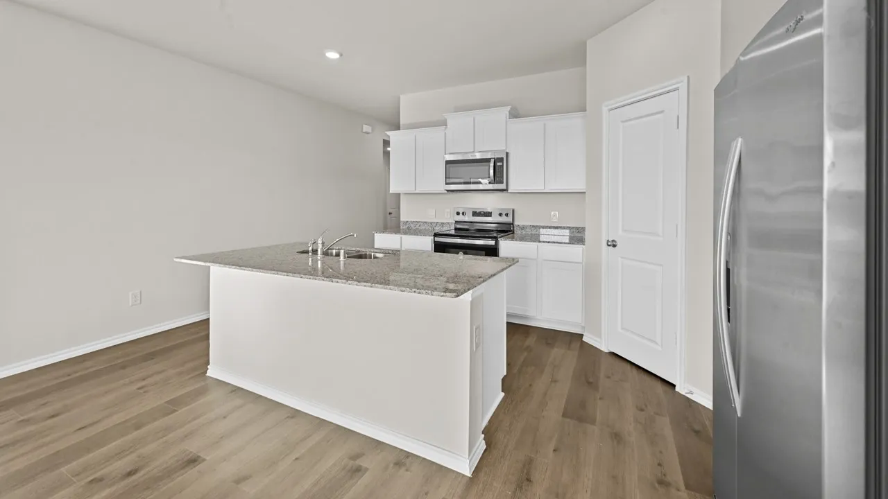 Kitchen featuring an island with a dual-basin stainless steel sink, granite countertops, white cabinetry, and stainless steel appliances including a microwave, range, and refrigerator