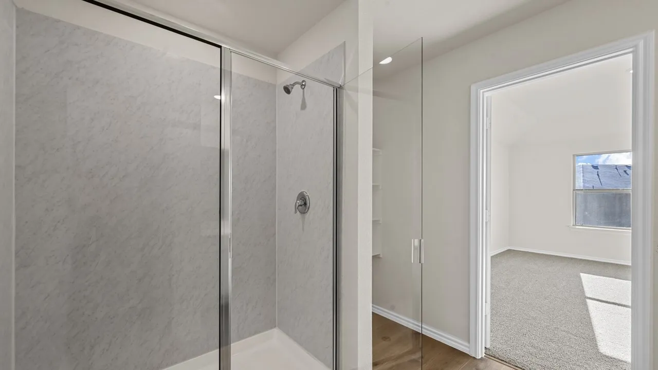Walk-in shower with clear glass enclosure and light-toned, textured wall panels