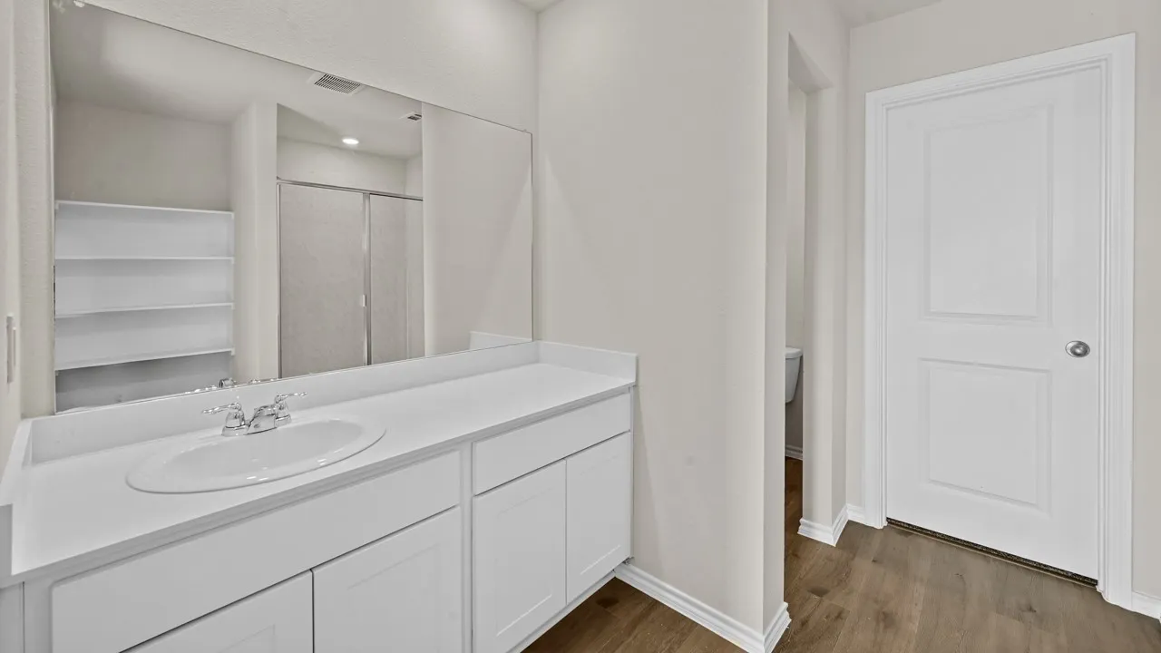 Bathroom vanity featuring a single basin sink, white cabinetry, a large mirror, and wood-finish flooring