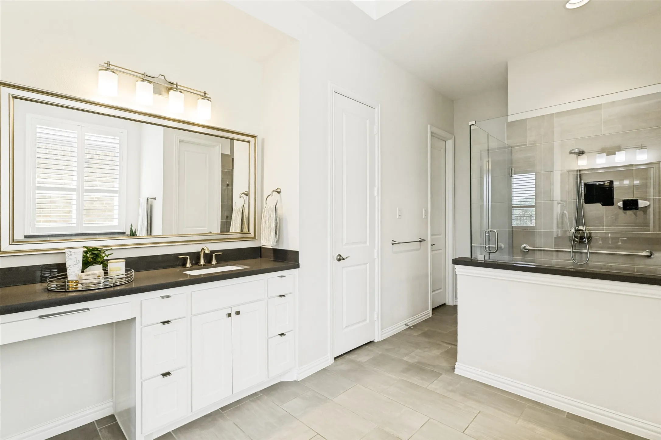 Bathroom featuring a spacious vanity with dark countertops, white cabinetry, undermount sink, and an expansive framed mirror