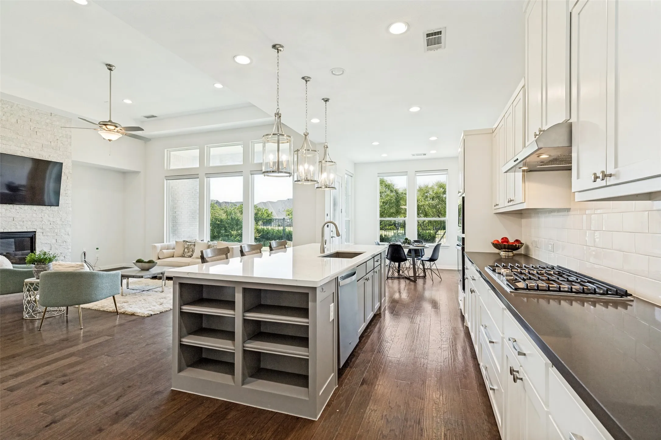 Spacious open-concept kitchen and living area featuring wood-finish flooring throughout, a large kitchen island with pendant lighting, white cabinetry, and a gas cooktop