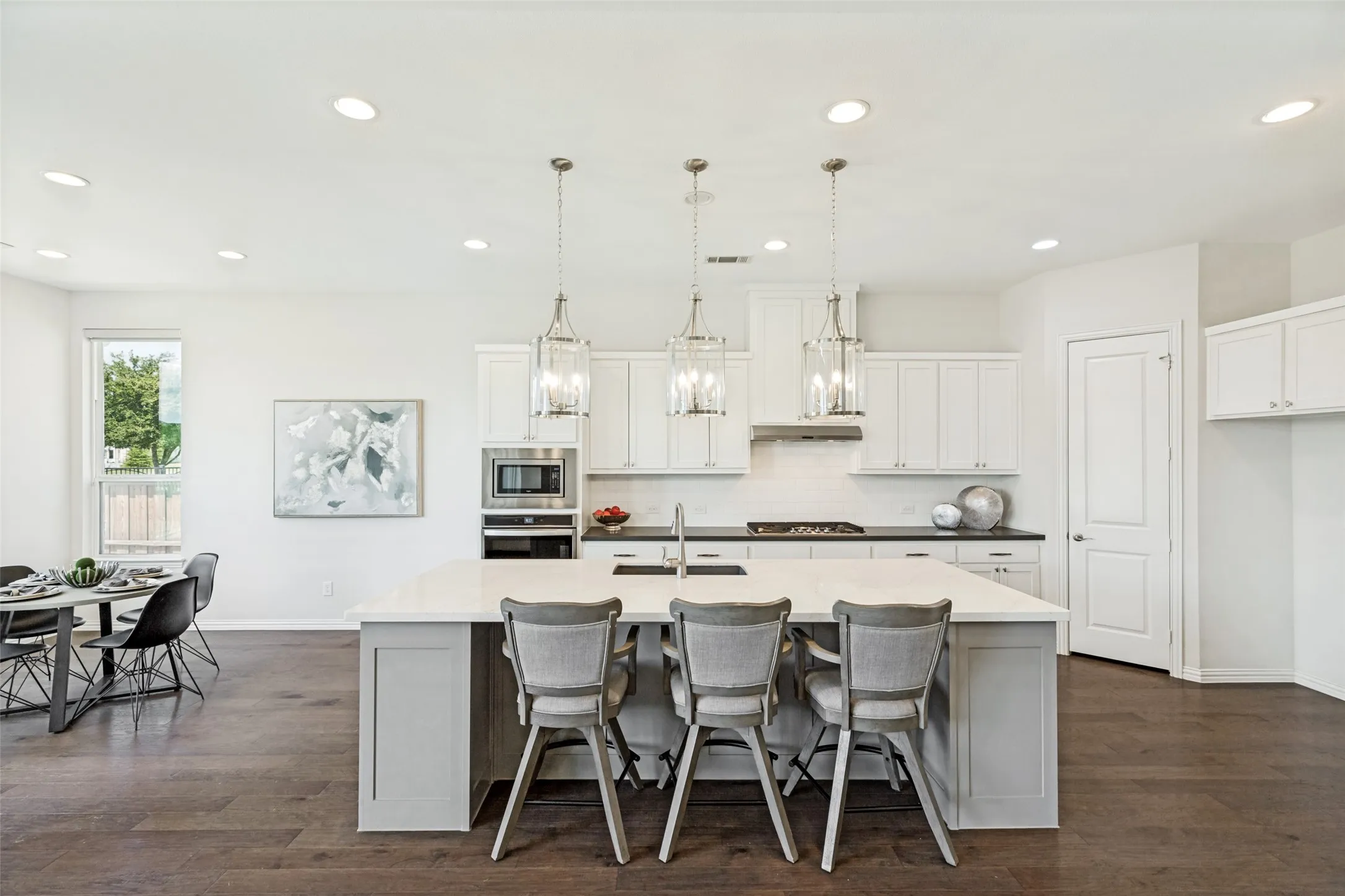 Open-concept kitchen featuring an oversized island with countertop seating, white shaker cabinetry, stainless steel appliances, and wood-finish flooring