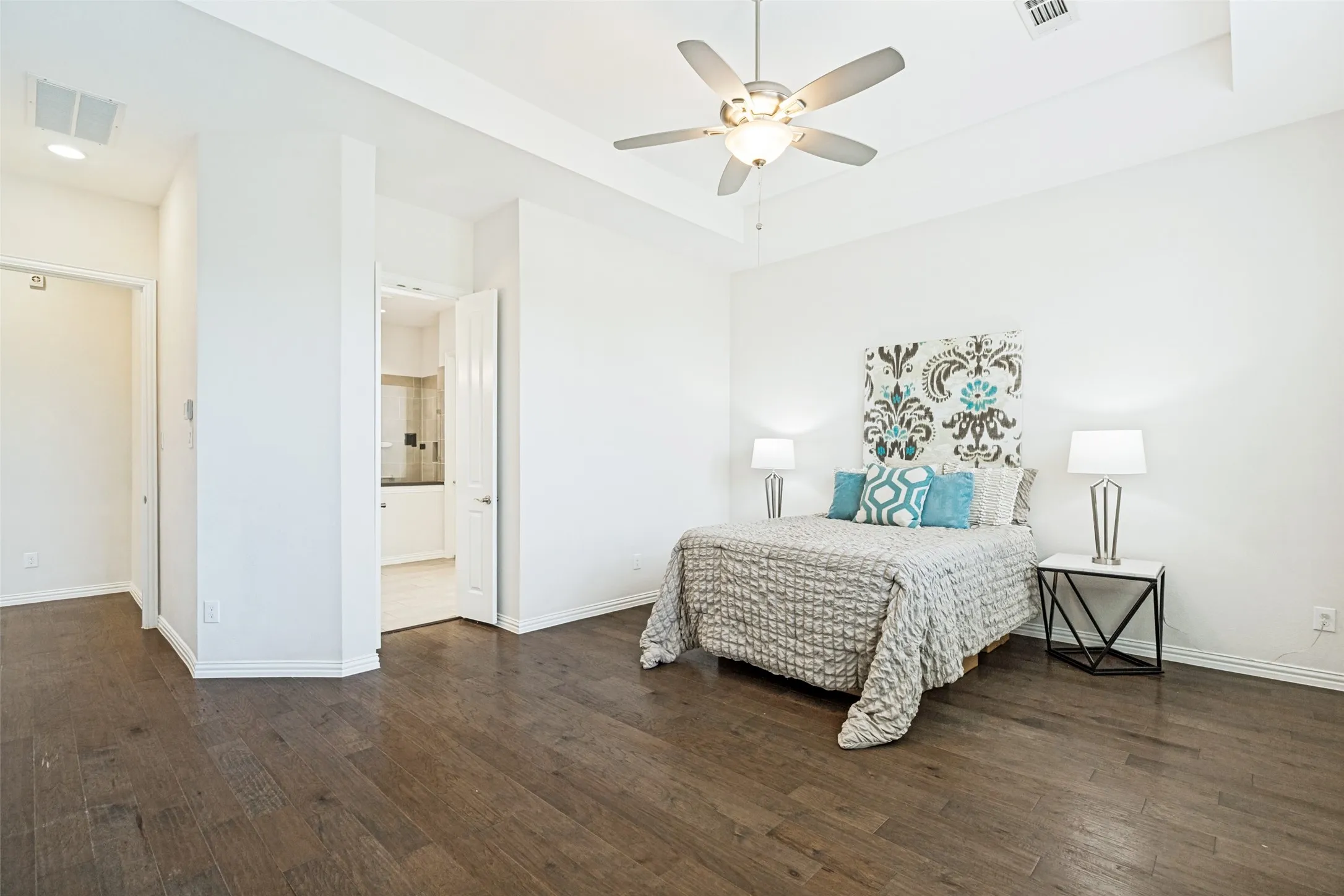 Spacious room featuring wood-finish flooring, a tray ceiling, and a ceiling fan with integrated lighting