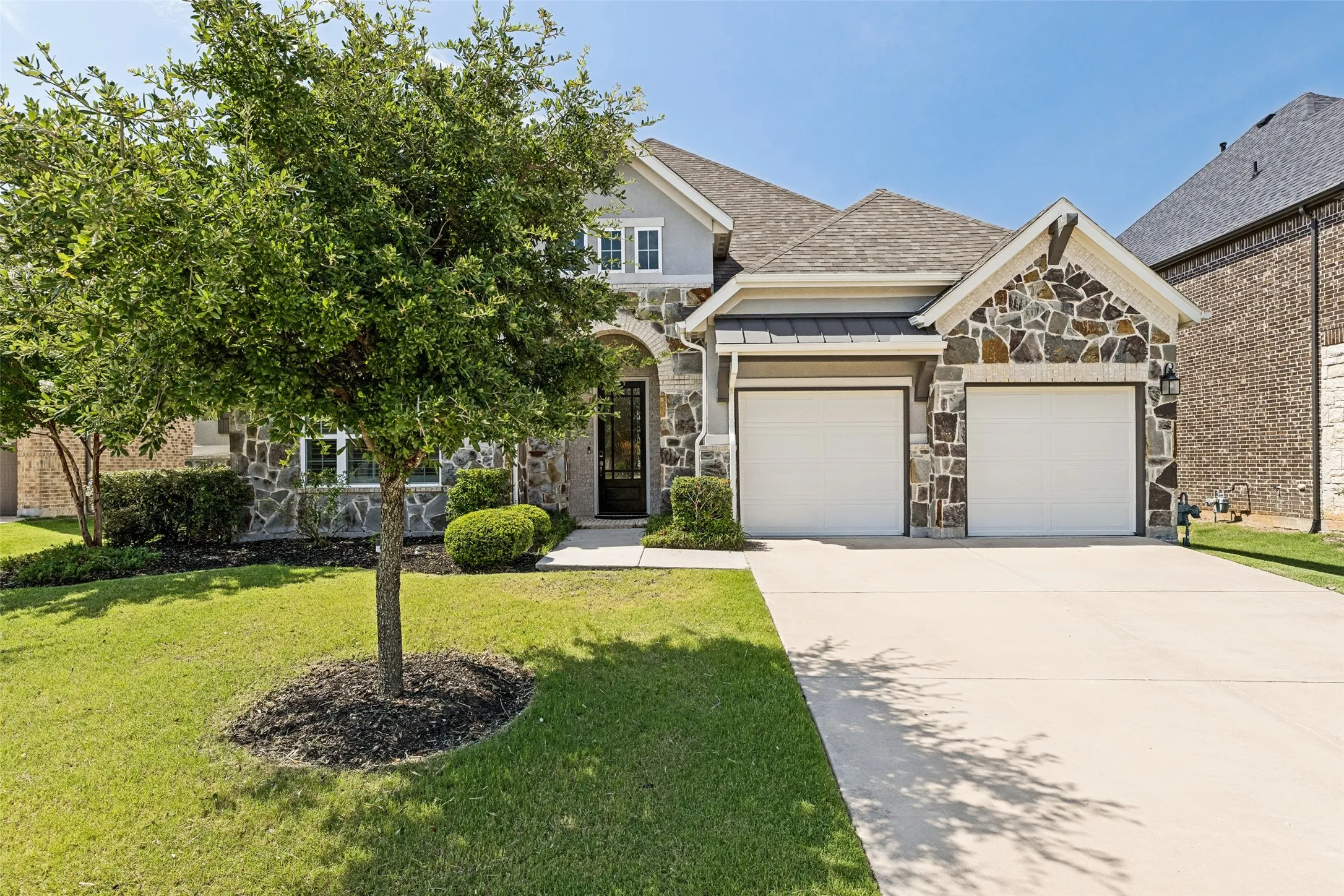 Stone and siding exterior with a dark-framed entry door, two-car garage, and concrete driveway