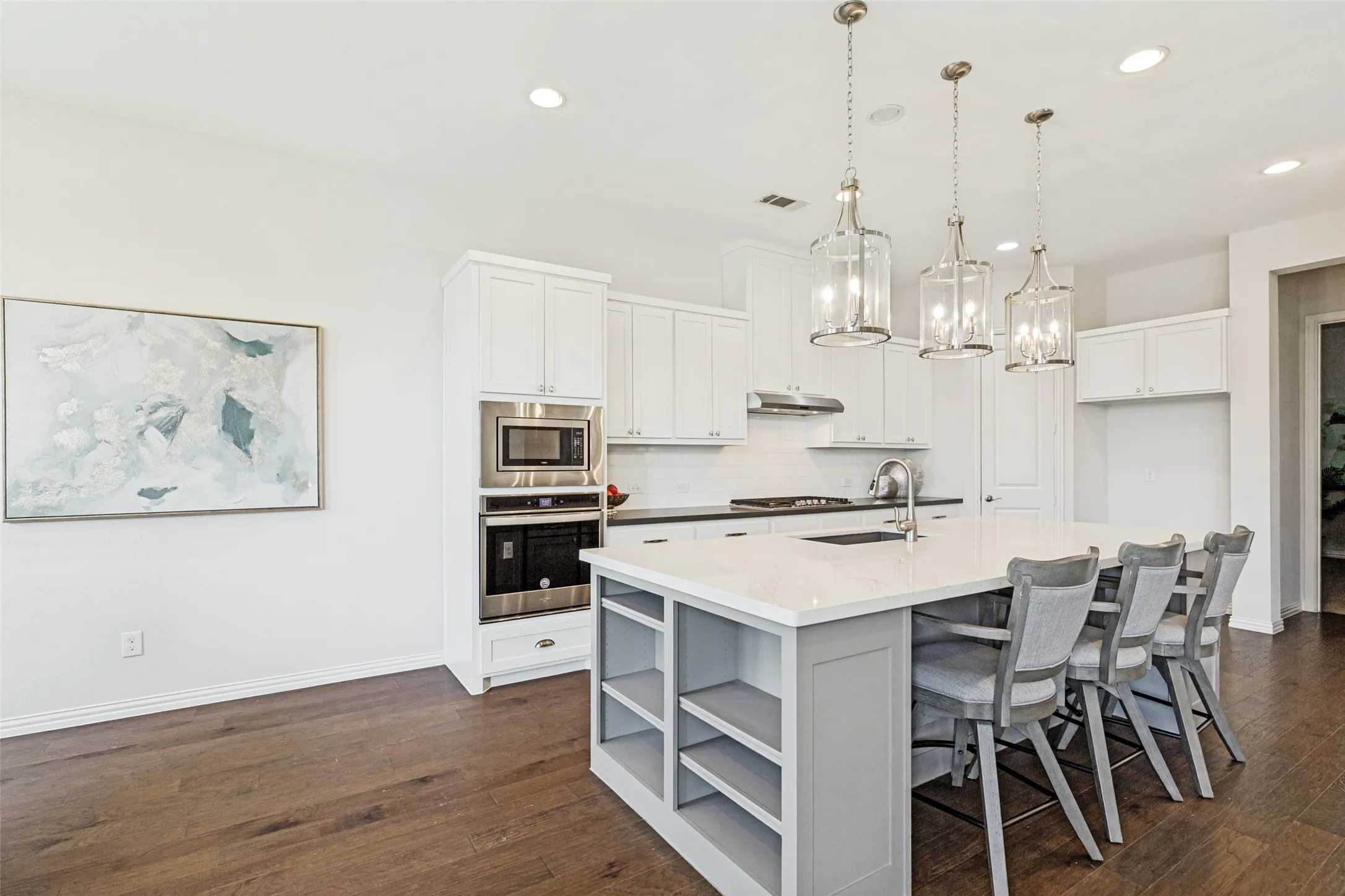 Modern kitchen featuring a large center island with integrated shelving, quartz countertops, stainless steel appliances, white cabinetry, and wood-finish flooring