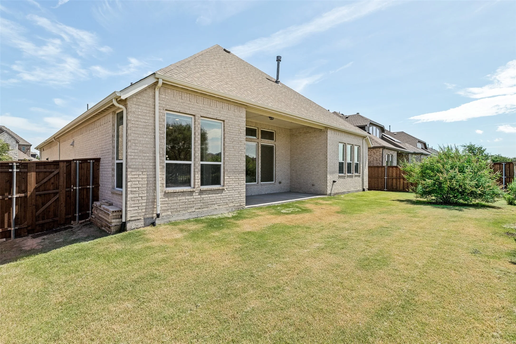 Expansive backyard featuring a manicured lawn, full brick exterior, large windows, covered patio, and privacy fencing