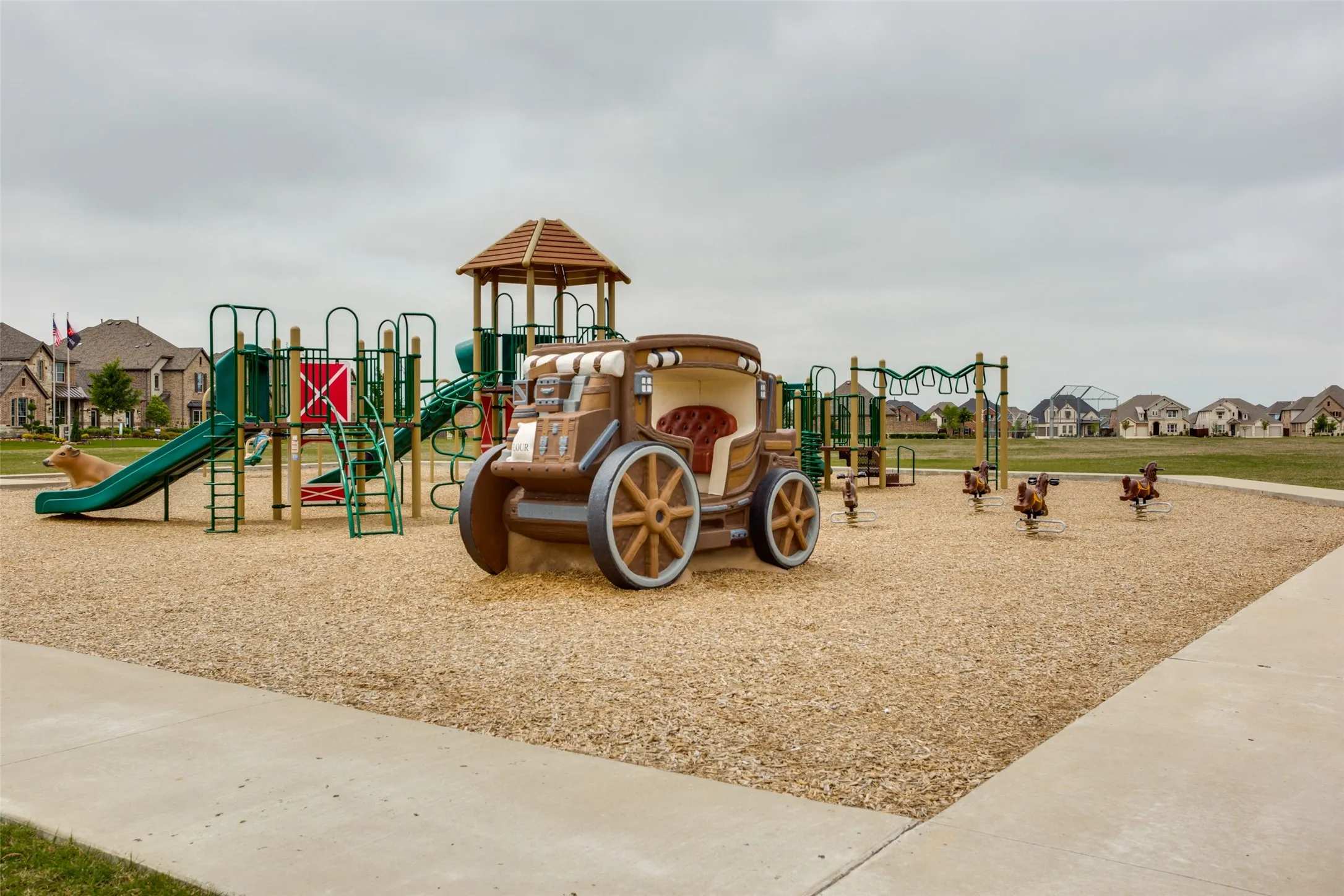 Community playground featuring multiple slides, climbing structures, a covered play tower, a decorative stagecoach, and spring riders