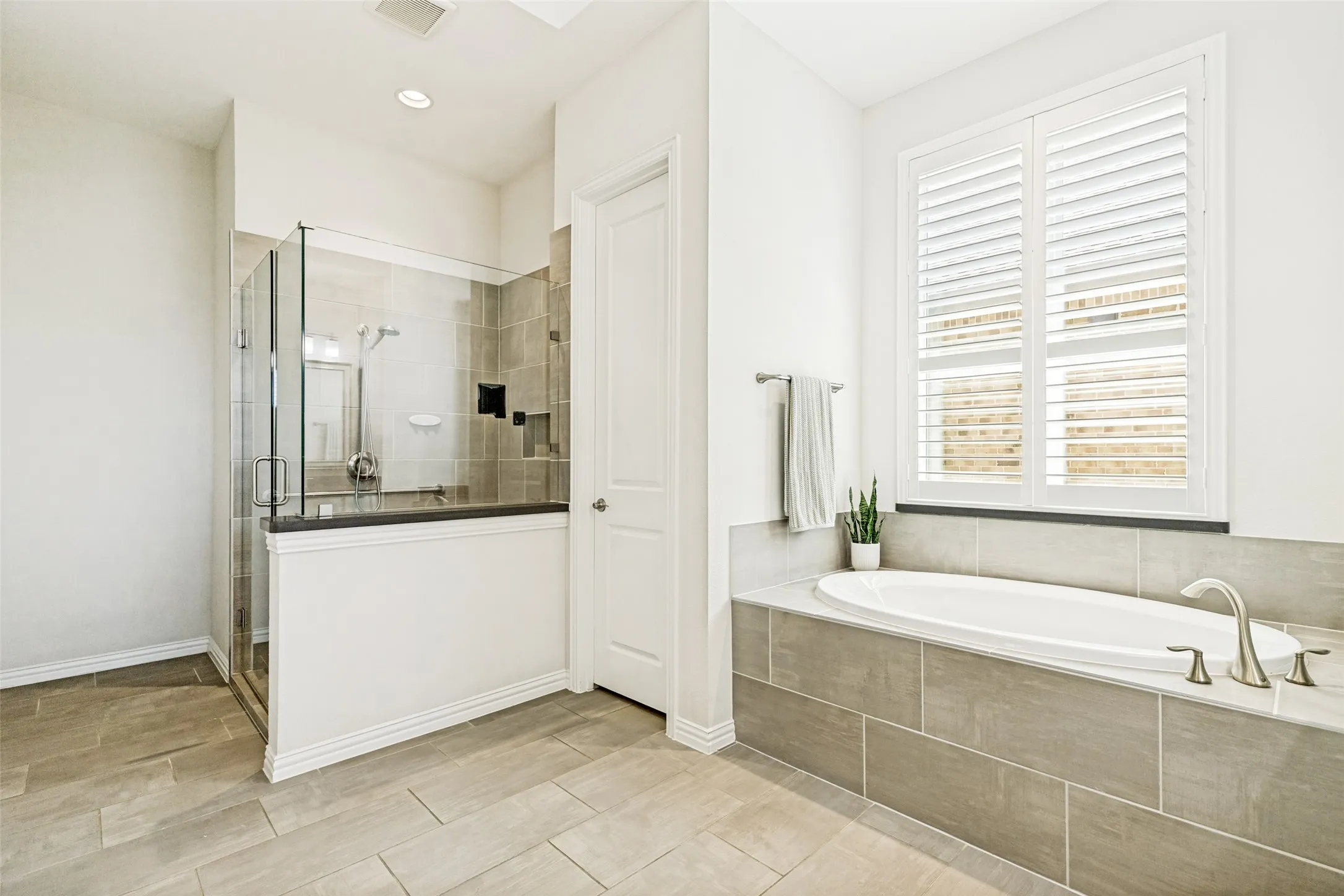 Spacious bathroom featuring a glass-enclosed shower, a large soaking tub with brushed nickel fixtures, and plantation shutters on the window