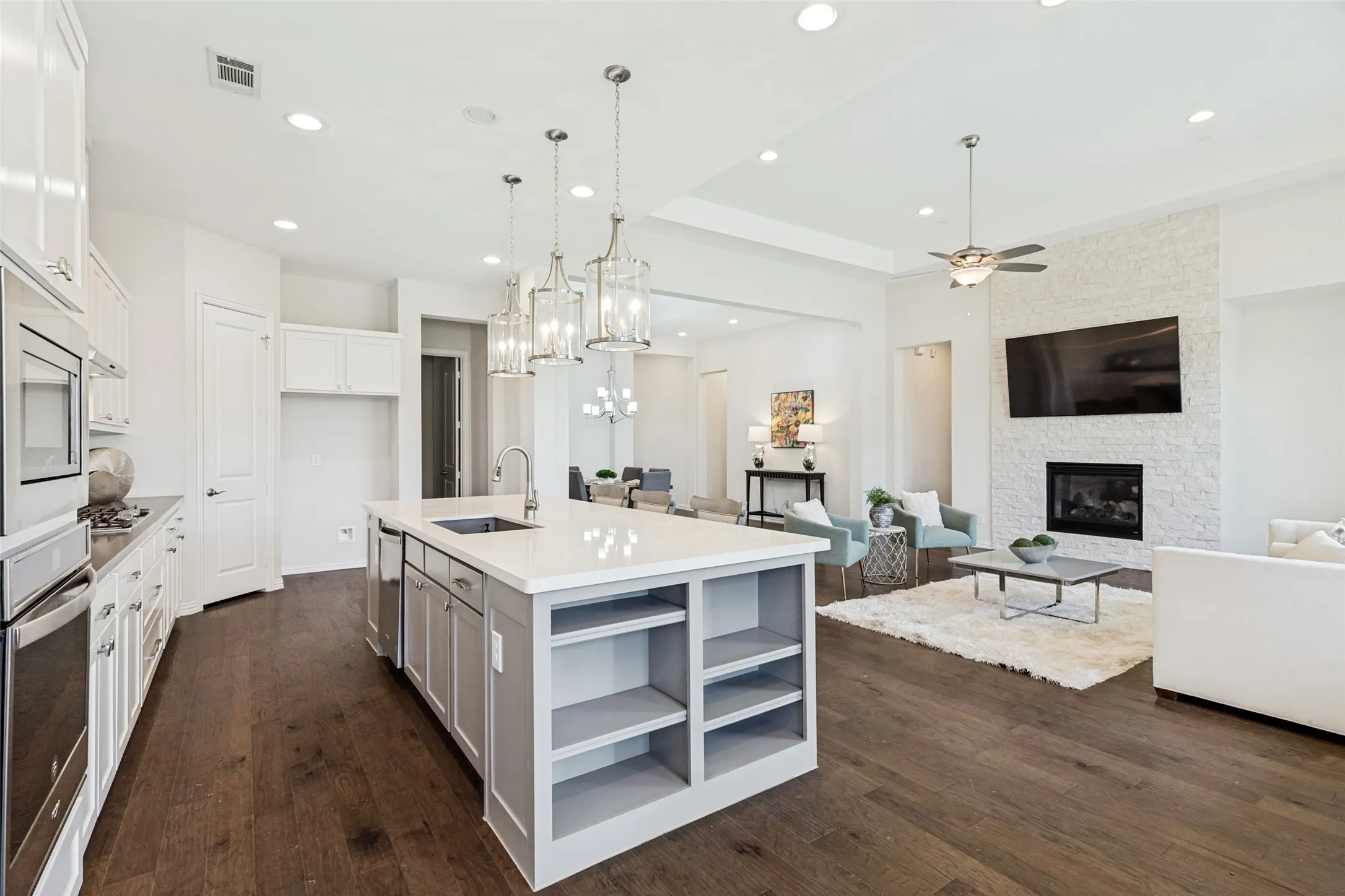 Open-concept living space with dark wood-finish flooring, recessed lighting, and a white tray ceiling