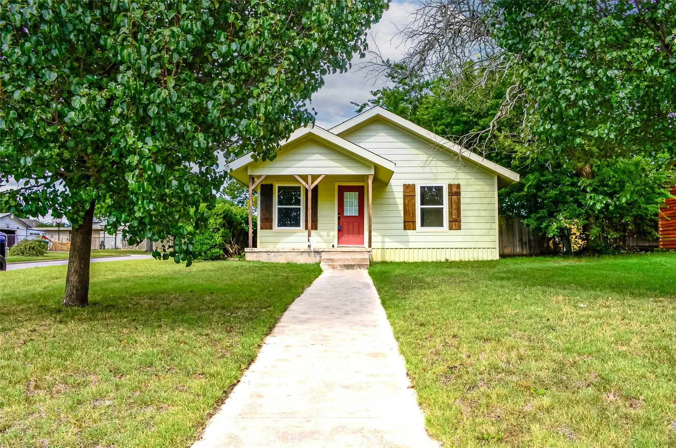 Light yellow siding exterior with a red entry door, framed by a concrete walkway