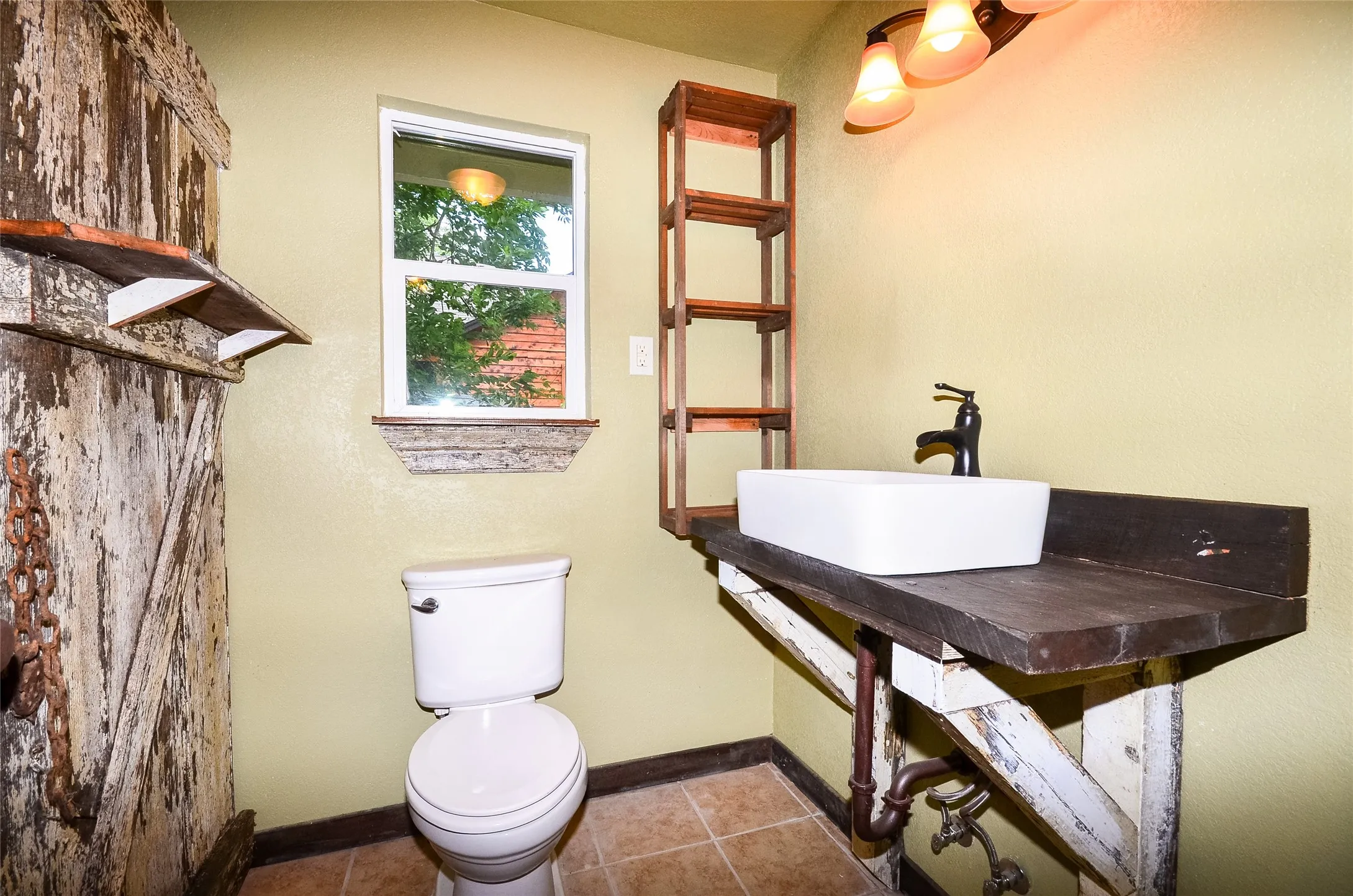 Bathroom featuring a vessel sink with a dark bronze faucet, a distressed wood vanity, and a window with a decorative sill