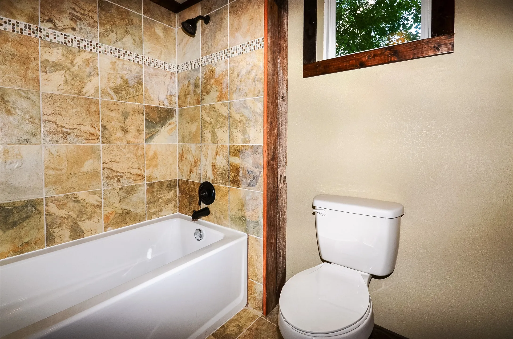 Bathtub with natural stone-look tile surround and mosaic accent band