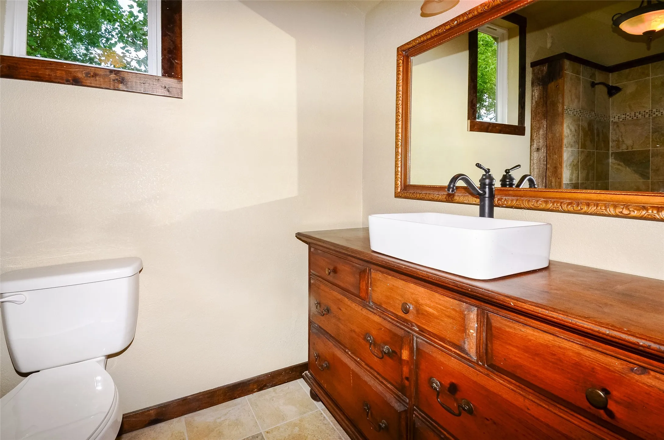 Bathroom featuring a vessel sink on a wood vanity with dark bronze fixtures, a framed mirror, and tiled flooring
