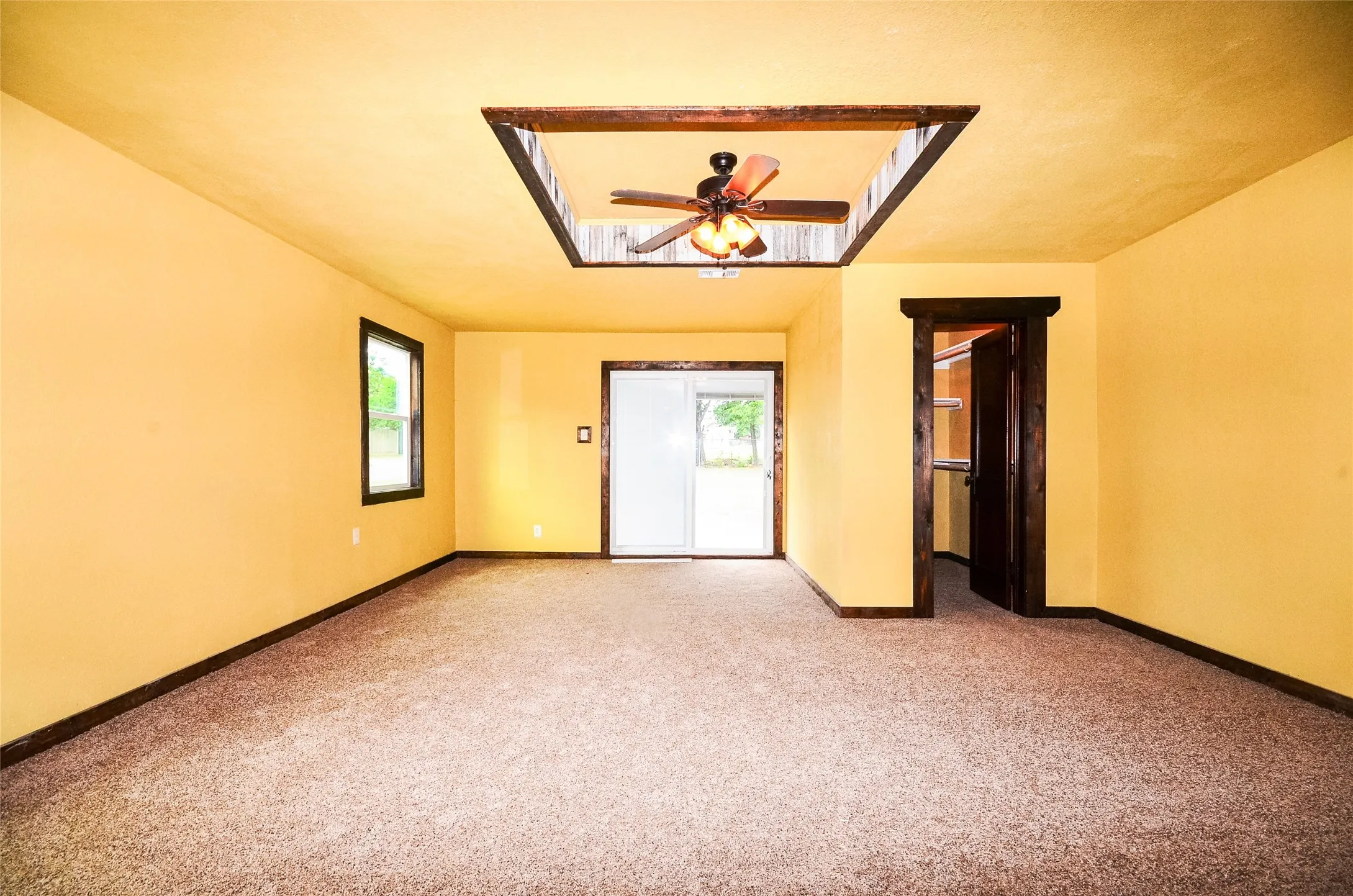 Recessed ceiling detail with a ceiling fan, carpeted flooring, and a sliding glass door