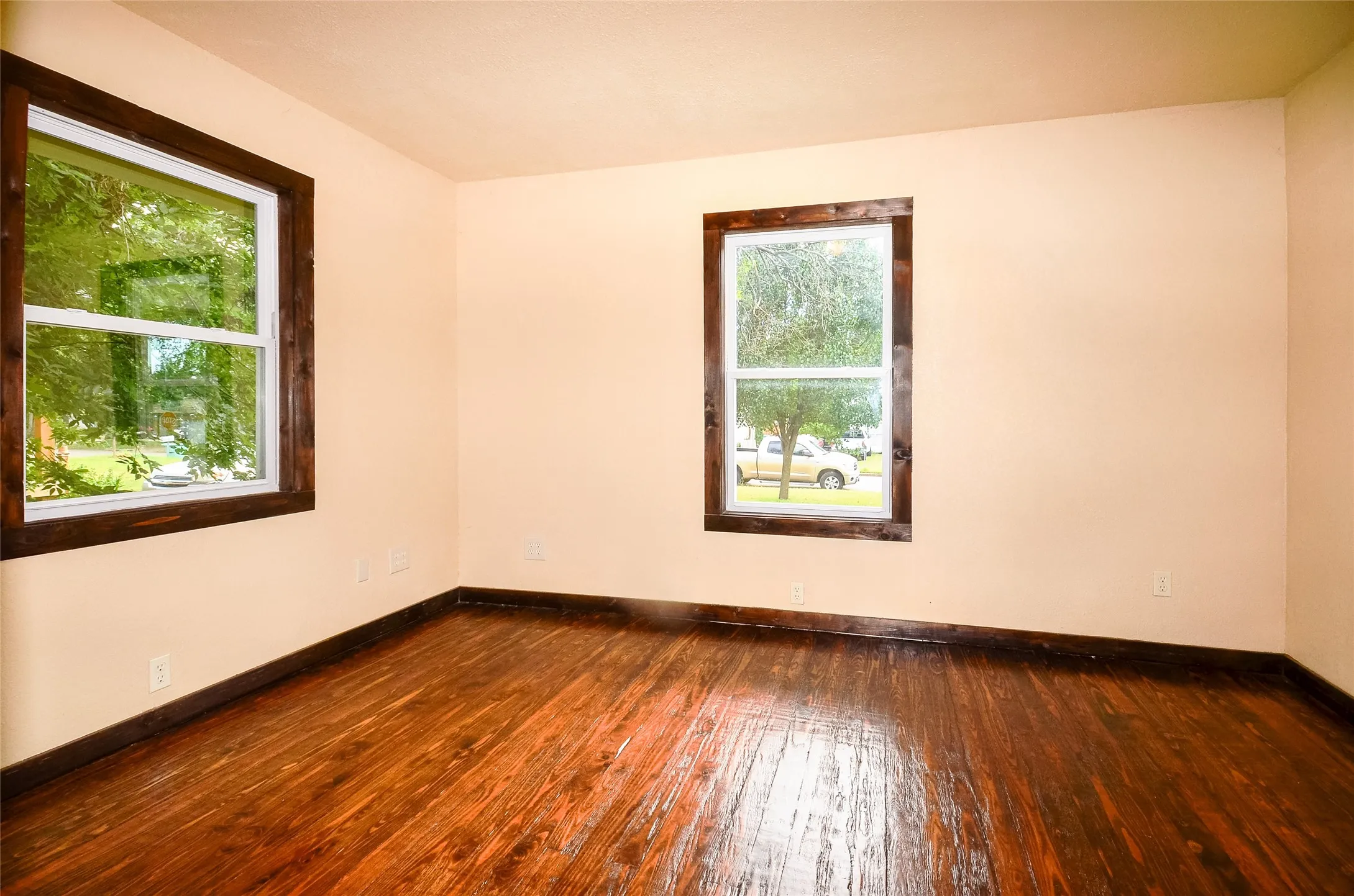 Interior room featuring wood-finish flooring, light-toned walls, and two windows with dark-stained wood trim