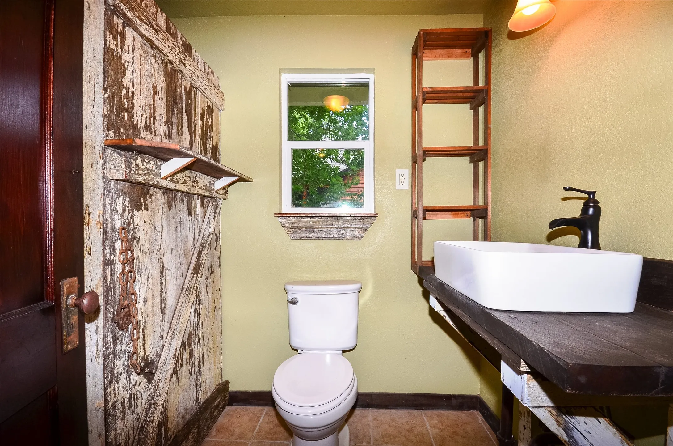Bathroom featuring a unique distressed wood barn door, vessel sink with a dark bronze faucet, custom wood vanity, and a window with a stone sill