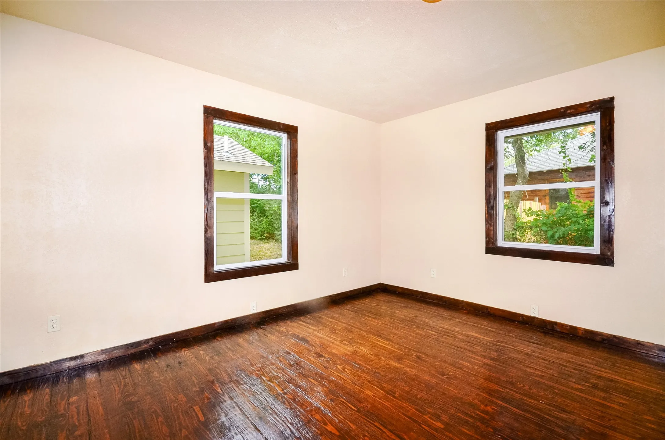 Room featuring rich wood-finish flooring, light-toned walls, and two windows with dark wood trim