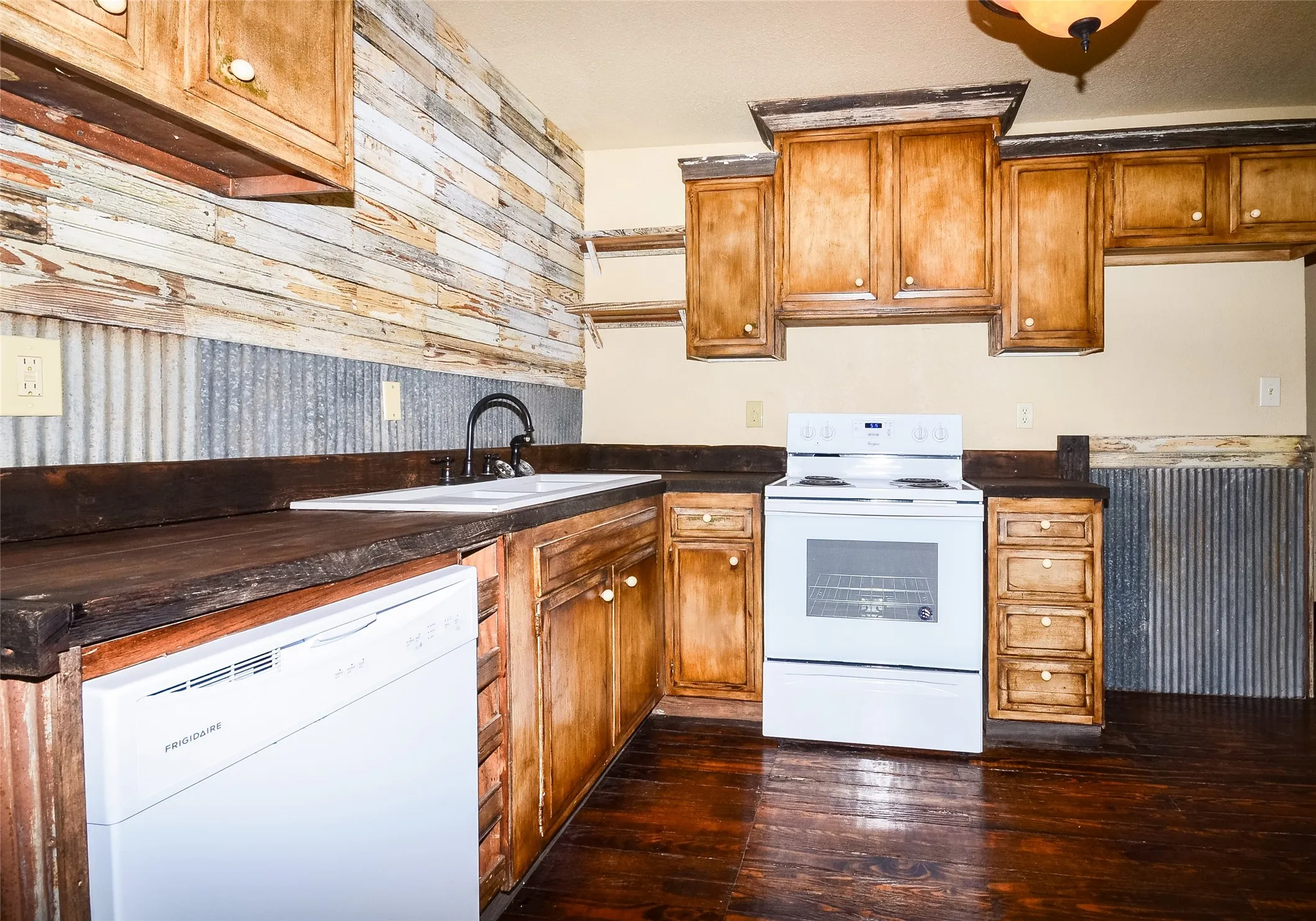Kitchen featuring wood-finish flooring, wood cabinetry with round pulls, white appliances, and a unique backsplash combining corrugated metal and horizontal wood paneling