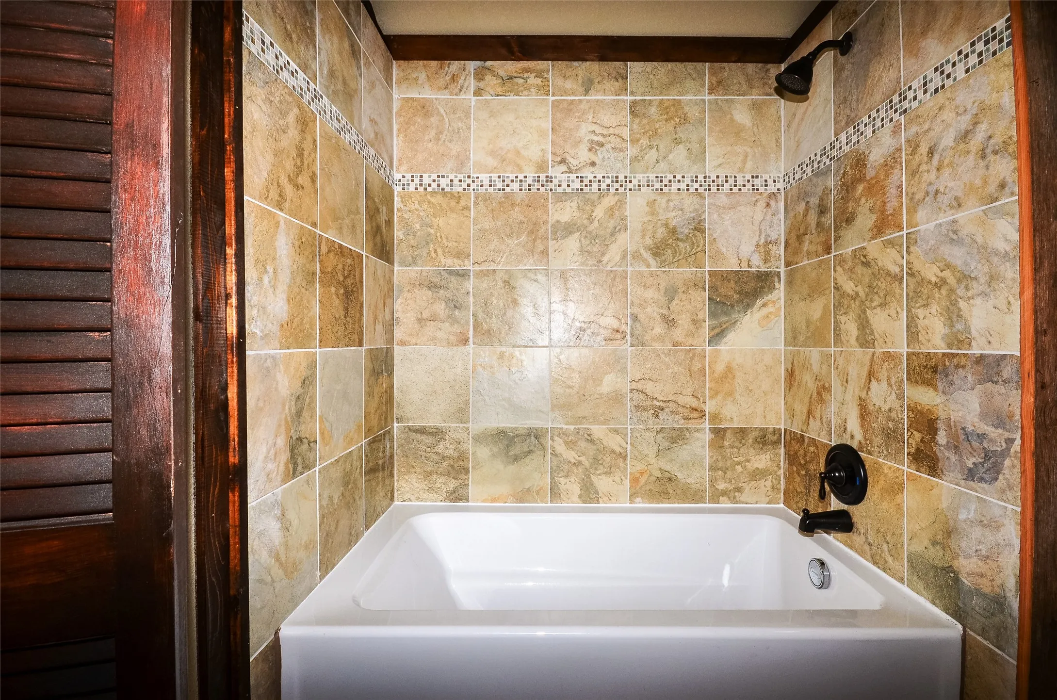 Bathtub with tiled surround featuring variegated square tiles and a mosaic accent band