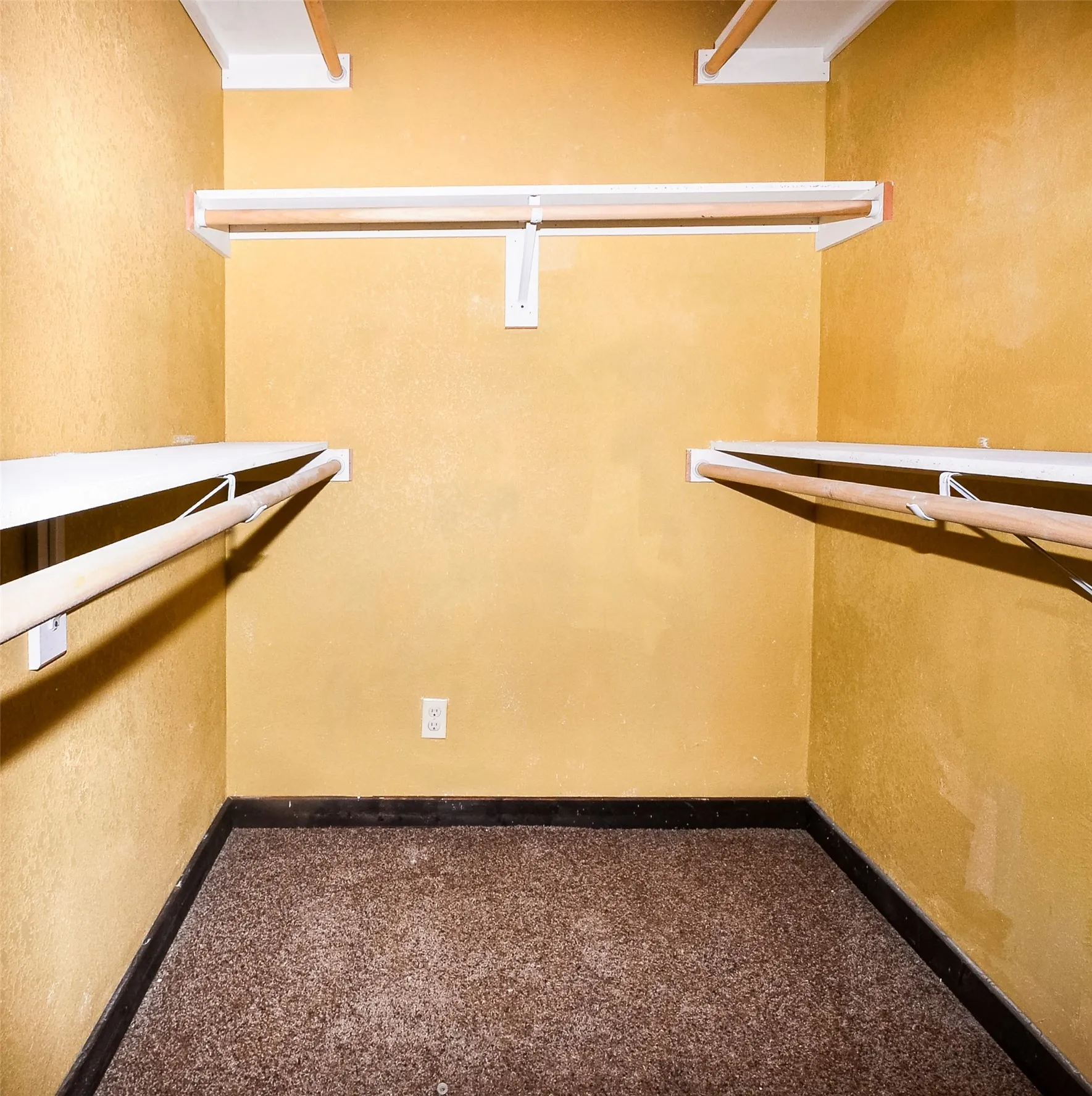 Walk-in closet featuring textured golden-yellow walls, multiple white shelving units, and wood-finish closet rods