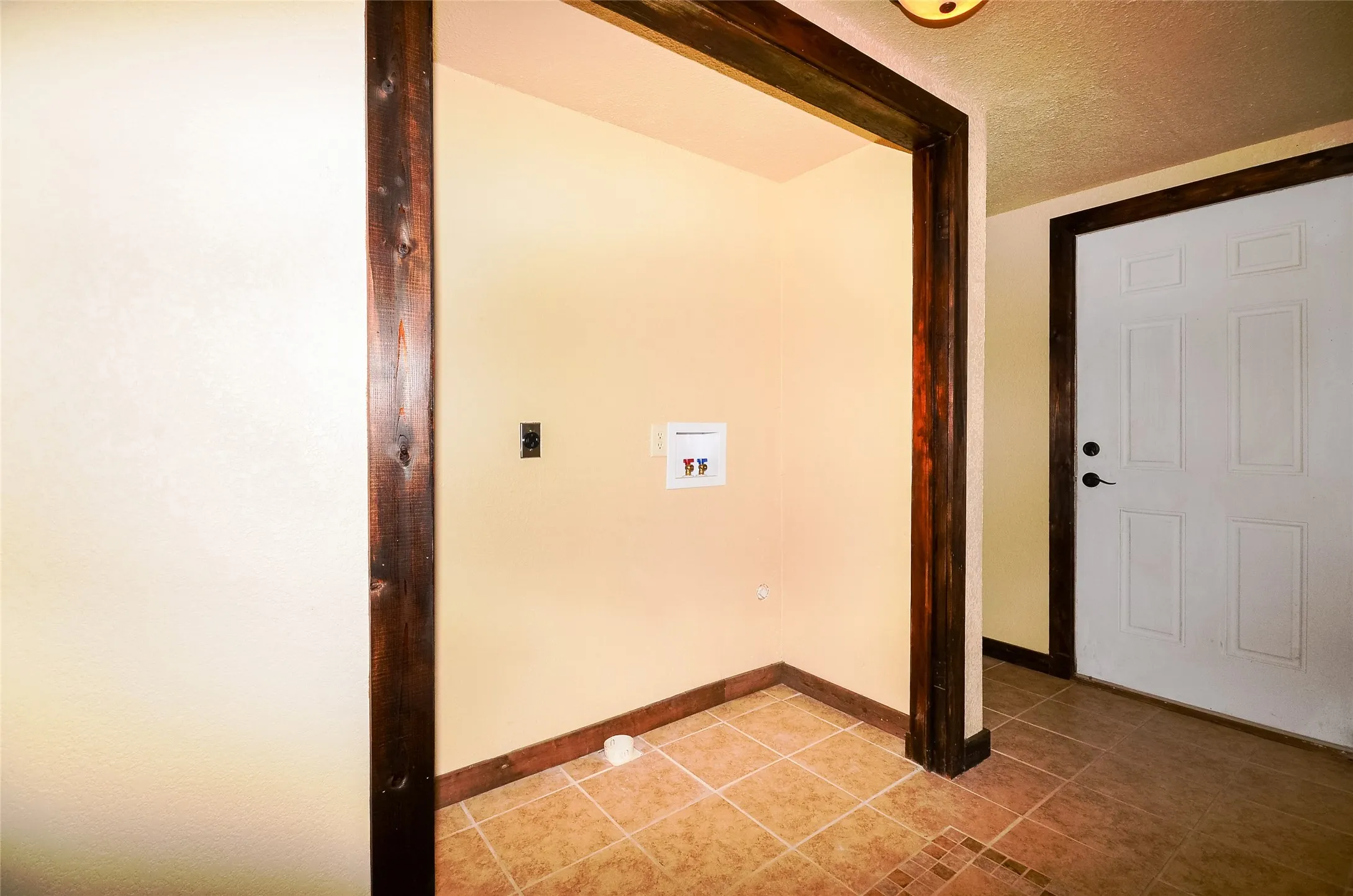 Utility alcove featuring wood-finish trim, tile flooring, and utility hookups