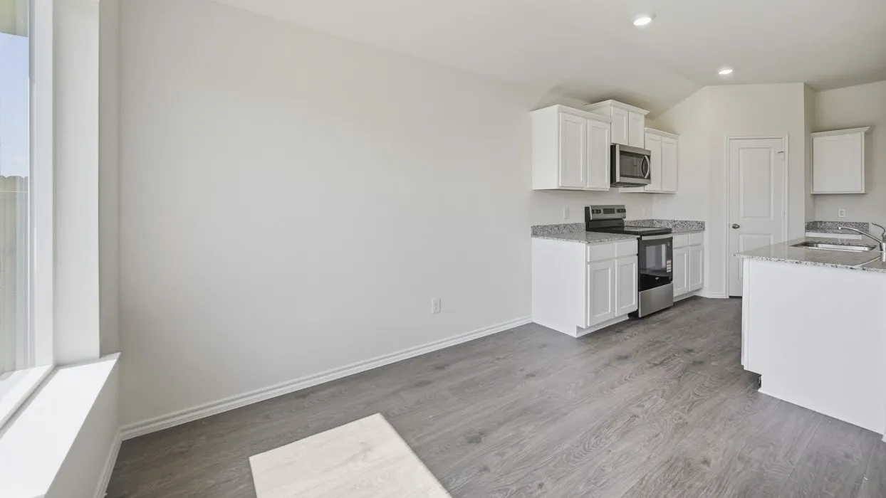 Open-concept kitchen area featuring white cabinetry, granite countertops, stainless steel appliances, and wood-finish flooring