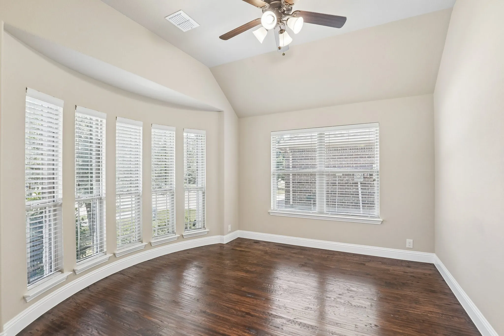 Room featuring a curved wall with five vertical windows, wood-finish flooring, an angled ceiling, and a ceiling fan with integrated lighting