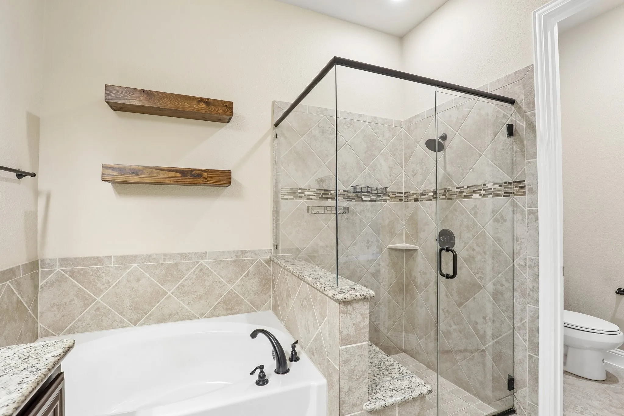 Bathroom featuring a built-in tub with dark bronze fixtures, a glass-enclosed shower with tile surround and decorative mosaic accent, and a built-in shower bench