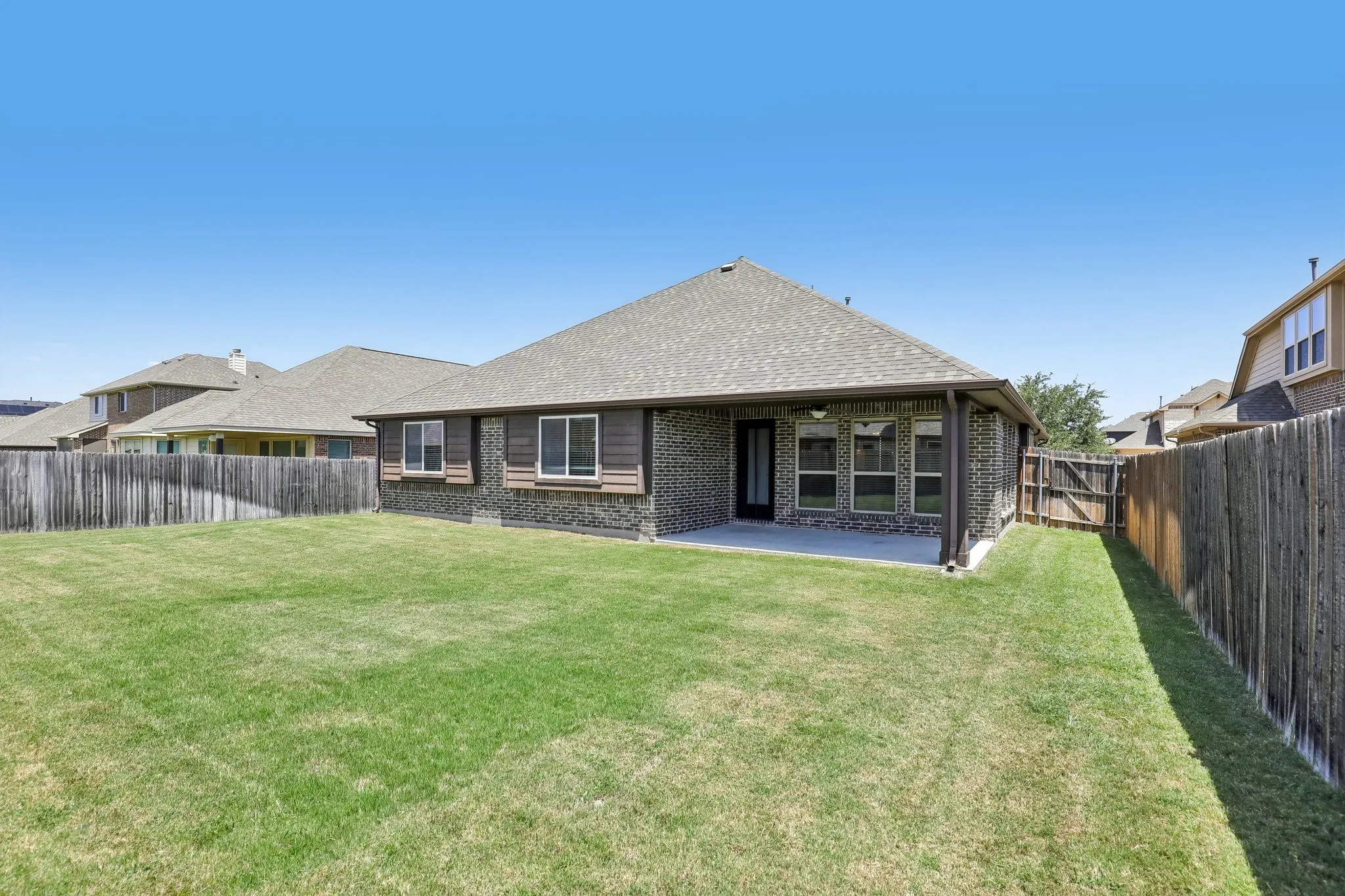 Expansive backyard featuring a green lawn, wood fence perimeter, and a covered concrete patio
