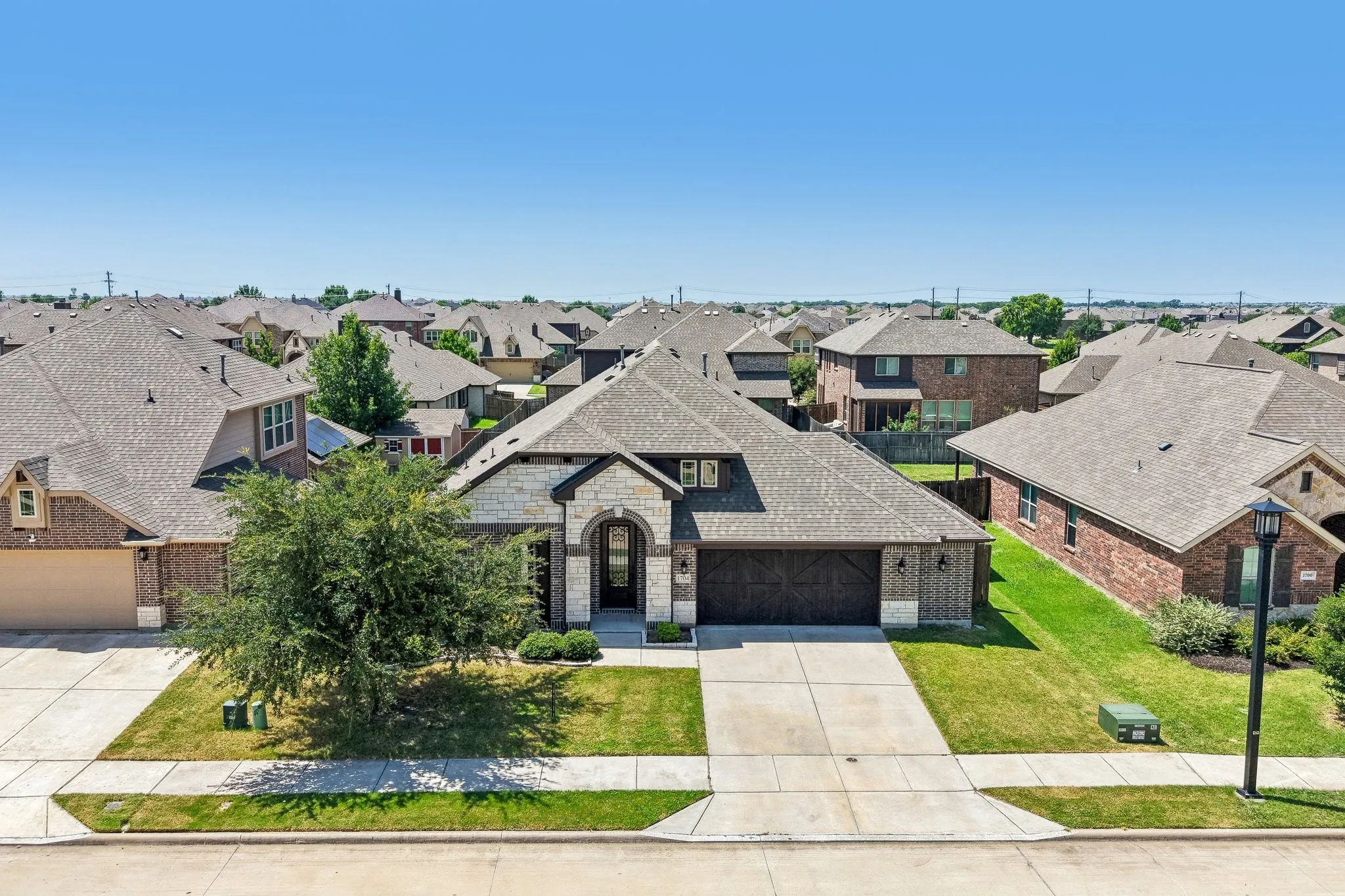 Single-story residence featuring a combination brick and stone facade, a dark wood-finish garage door, and an arched entry