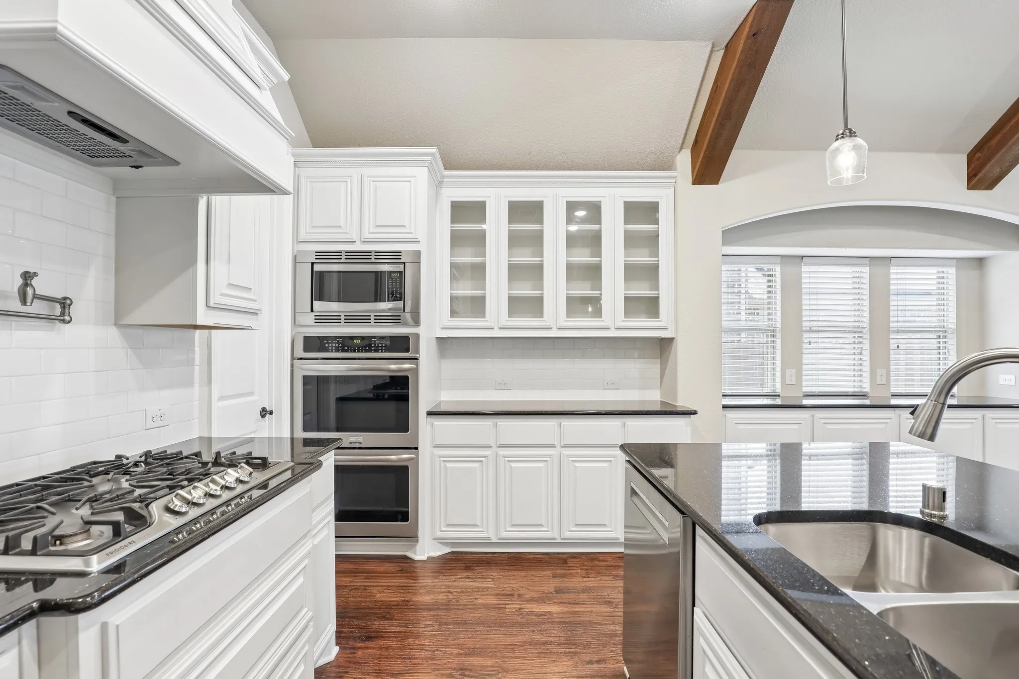 Kitchen featuring white cabinetry, dark stone countertops, stainless steel appliances, wood-finish flooring, and exposed ceiling beams