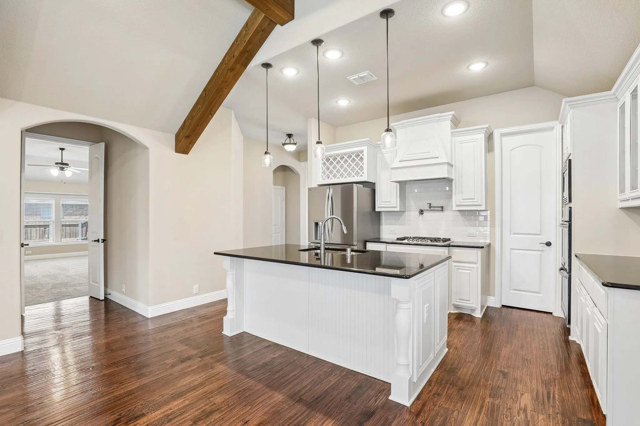 Open-concept kitchen featuring an island with a dark countertop and pendant lighting, white cabinetry, stainless steel appliances, and wood-finish flooring