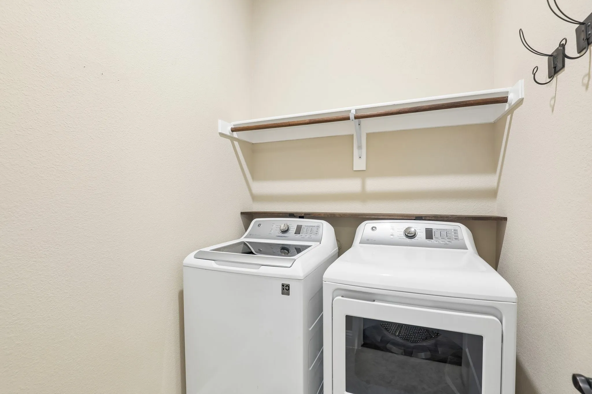 Dedicated laundry area featuring a white hanging shelf with a wood-finish rod, a wood-finish counter, and textured cream walls