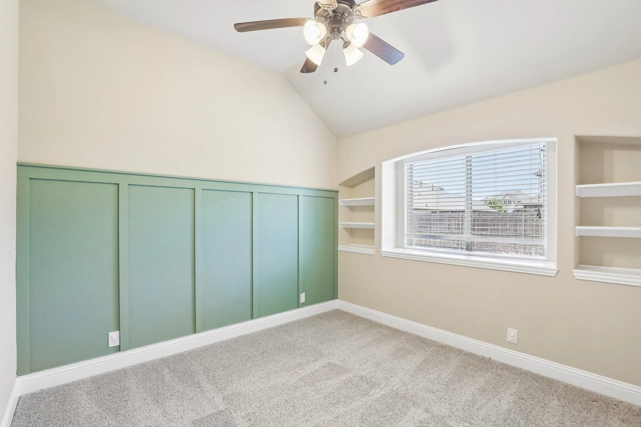 Vaulted ceiling room featuring a decorative board and batten wall accent, built-in shelving, a window with horizontal blinds, and a ceiling fan with integrated lighting
