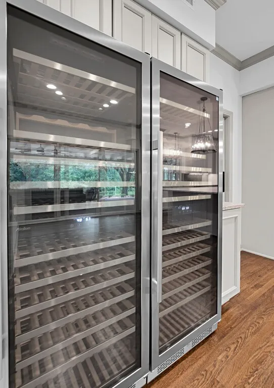 Integrated dual-zone wine refrigeration system with glass doors and wood-finish shelving, set within custom cabinetry featuring paneled doors, crown molding, and wood-finish flooring
