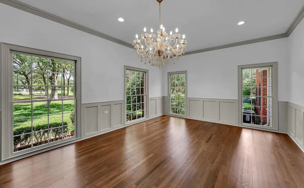 Hardwood flooring throughout this spacious room, featuring neutral wall paint, wainscoting, and crown molding