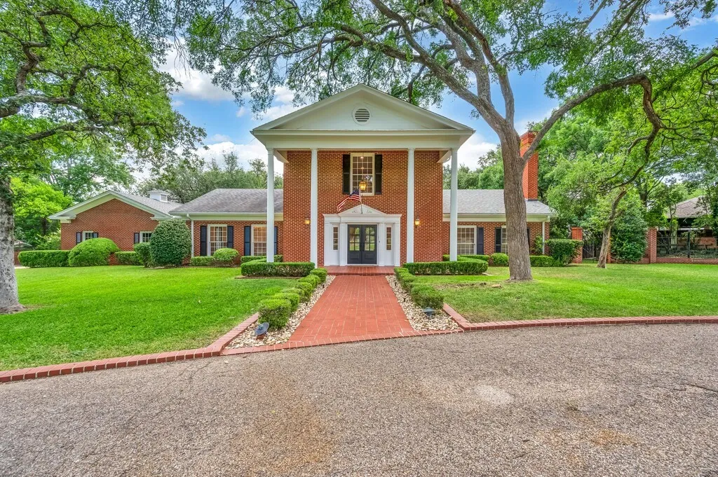 Classical brick residence featuring a prominent columned portico, a black double-entry door, and a red brick pathway