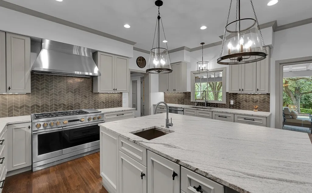 Gourmet kitchen featuring a large central island with an undermount sink, light-toned countertops, and custom cabinetry with dark hardware