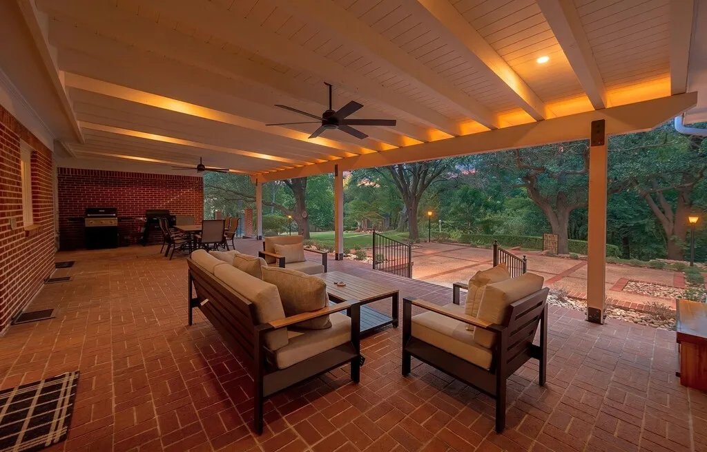 Expansive covered patio featuring brick-laid flooring, exposed beam ceiling with recessed lighting, and dual ceiling fans