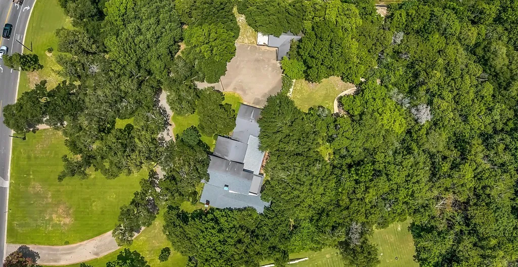 Expansive property featuring a multi-level roofline, extensive mature tree cover, and a large paved parking area
