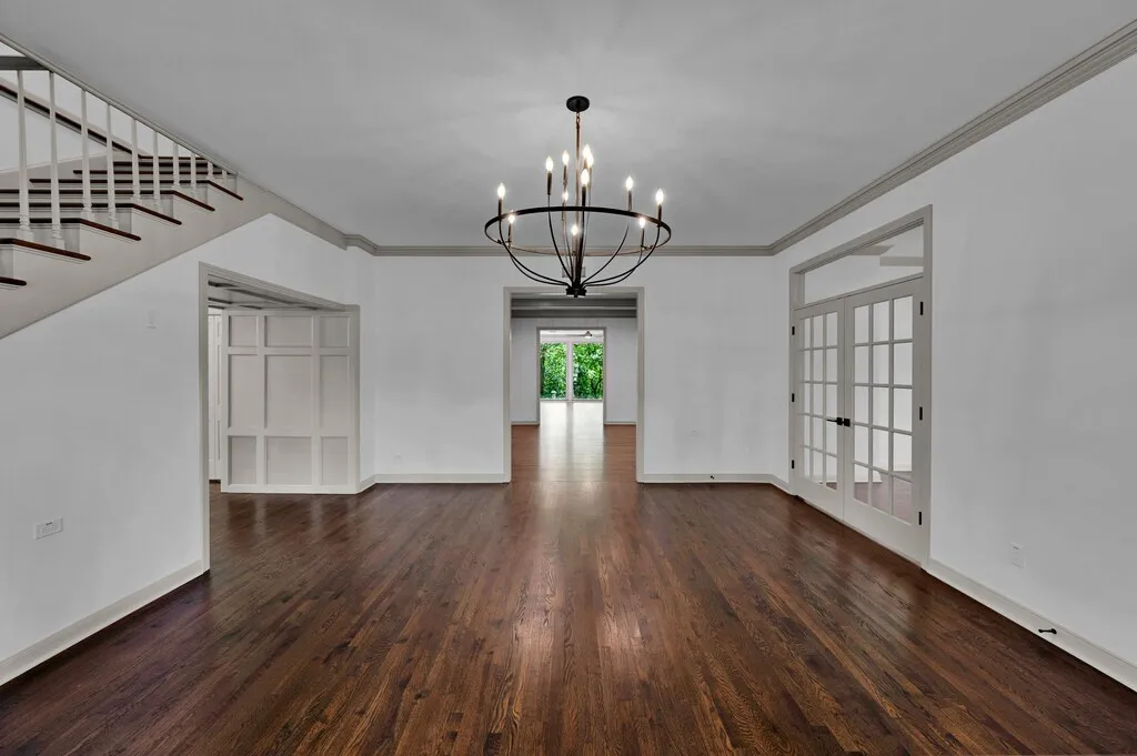 Spacious room featuring rich wood-finish flooring, a contemporary black metal chandelier, white walls with gray crown molding, and a staircase with white risers and dark wood treads