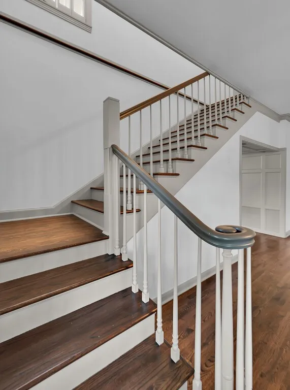 Staircase featuring wood-finish treads and risers, a white baluster system, and a dark handrail with a decorative scroll newel post