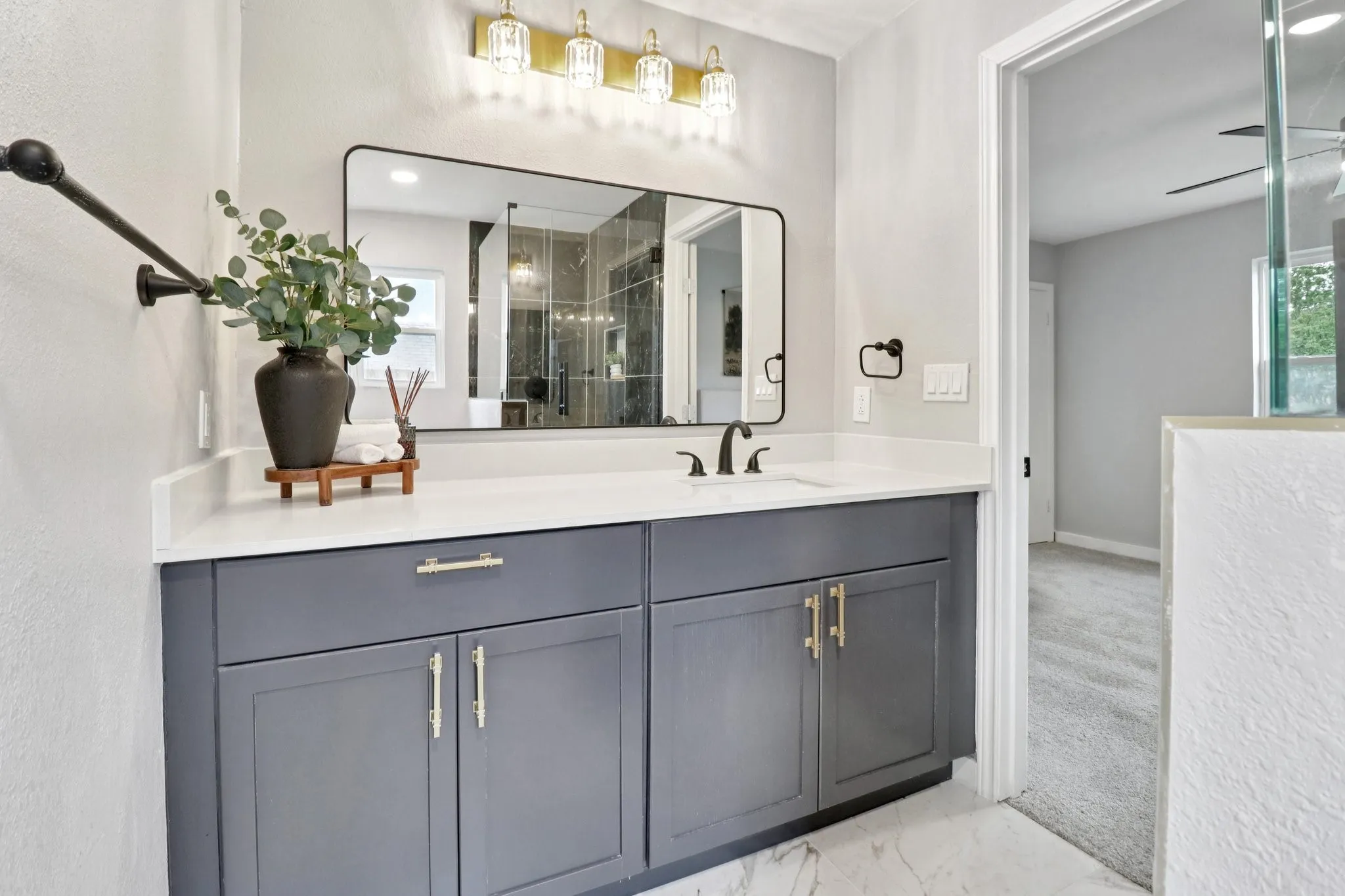 Contemporary vanity featuring a white countertop, matte gray cabinetry with gold-finish hardware, and a rectangular black-framed mirror
